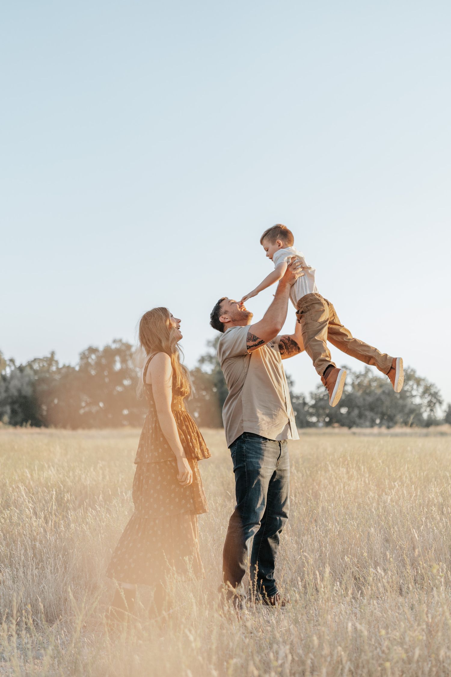 Couple spinning and dancing together joyfully in a sunlit meadow with tall golden grass at sunset.