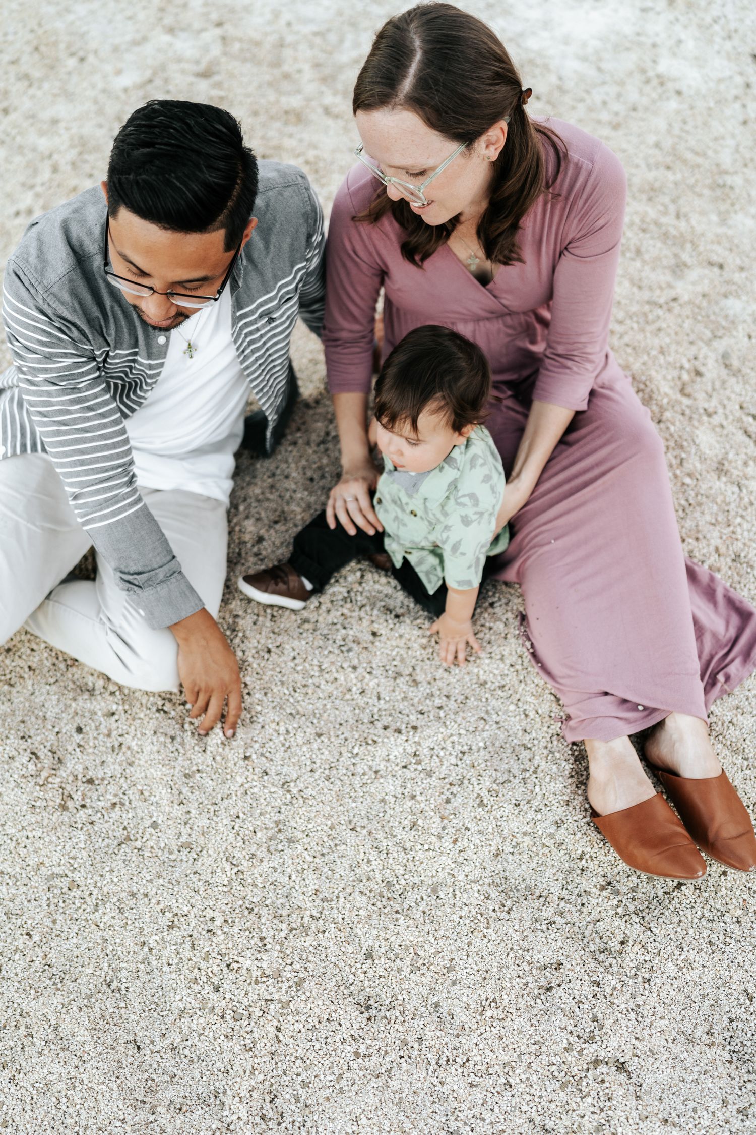 A family in coordinated outfits sits together on a sandy beach looking down at something.
