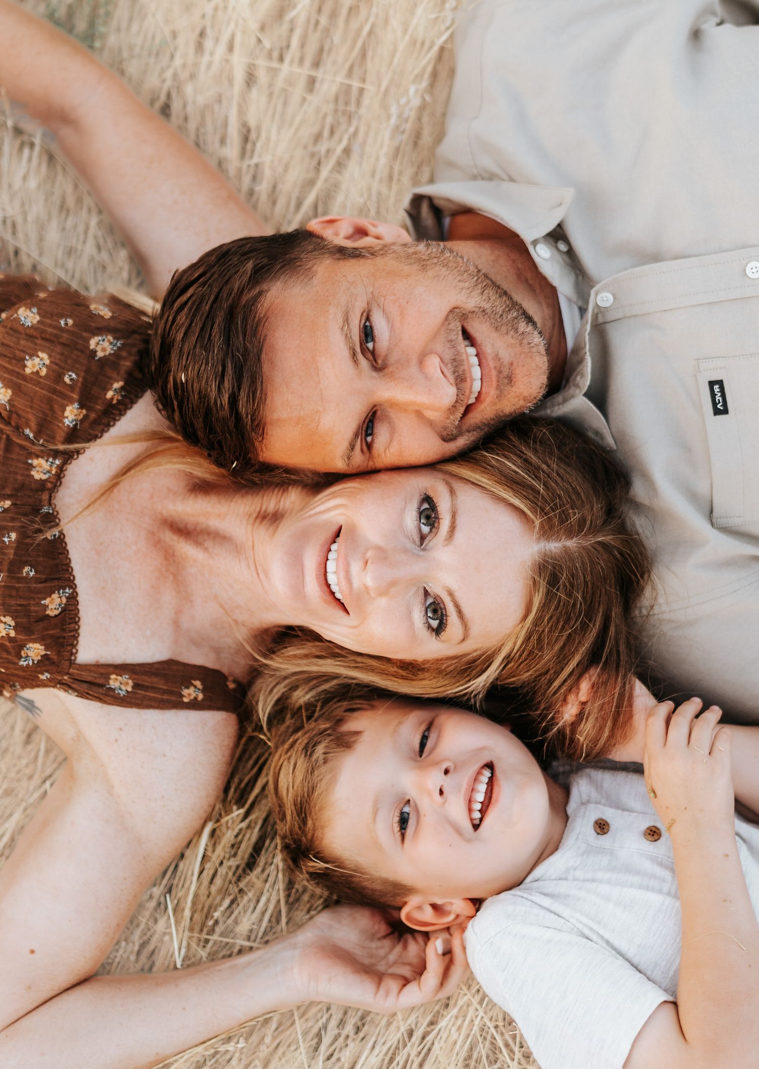 An intimate family portrait lying in golden wheat field with joyful expressions.