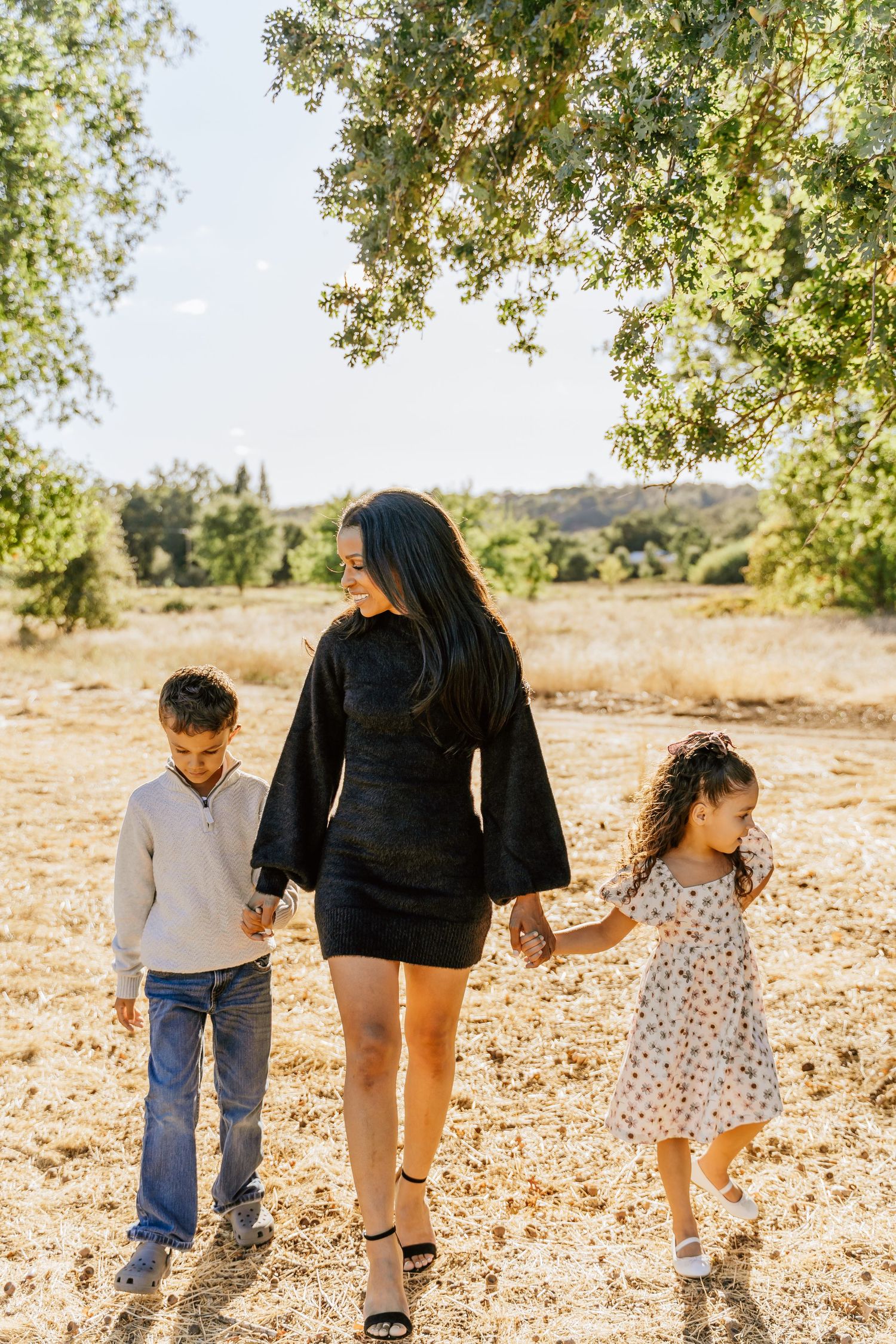 Family members holding hands while walking together on a dirt path under shady trees.