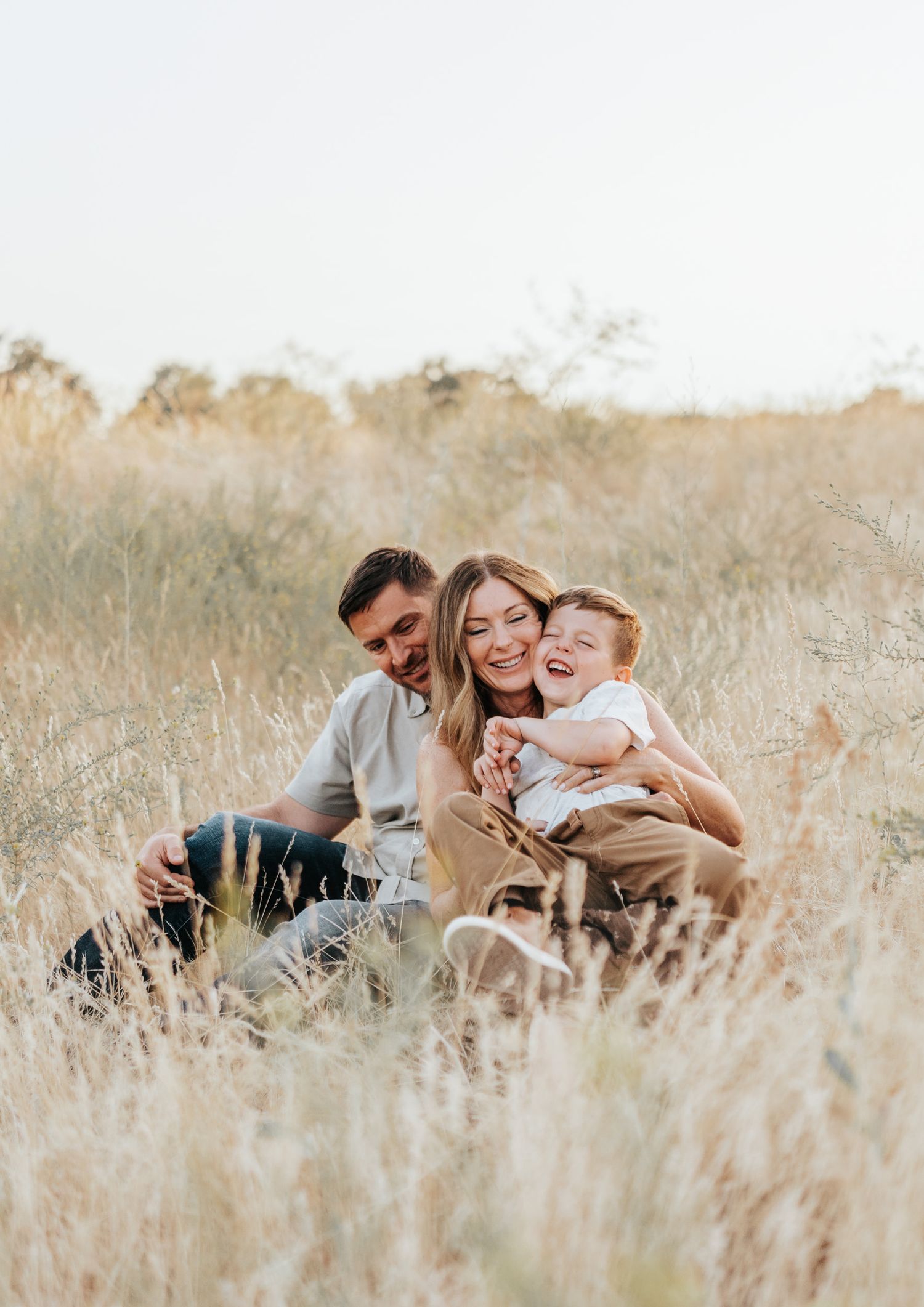 A group sits together laughing in tall golden grass during a warm sunset photo session.