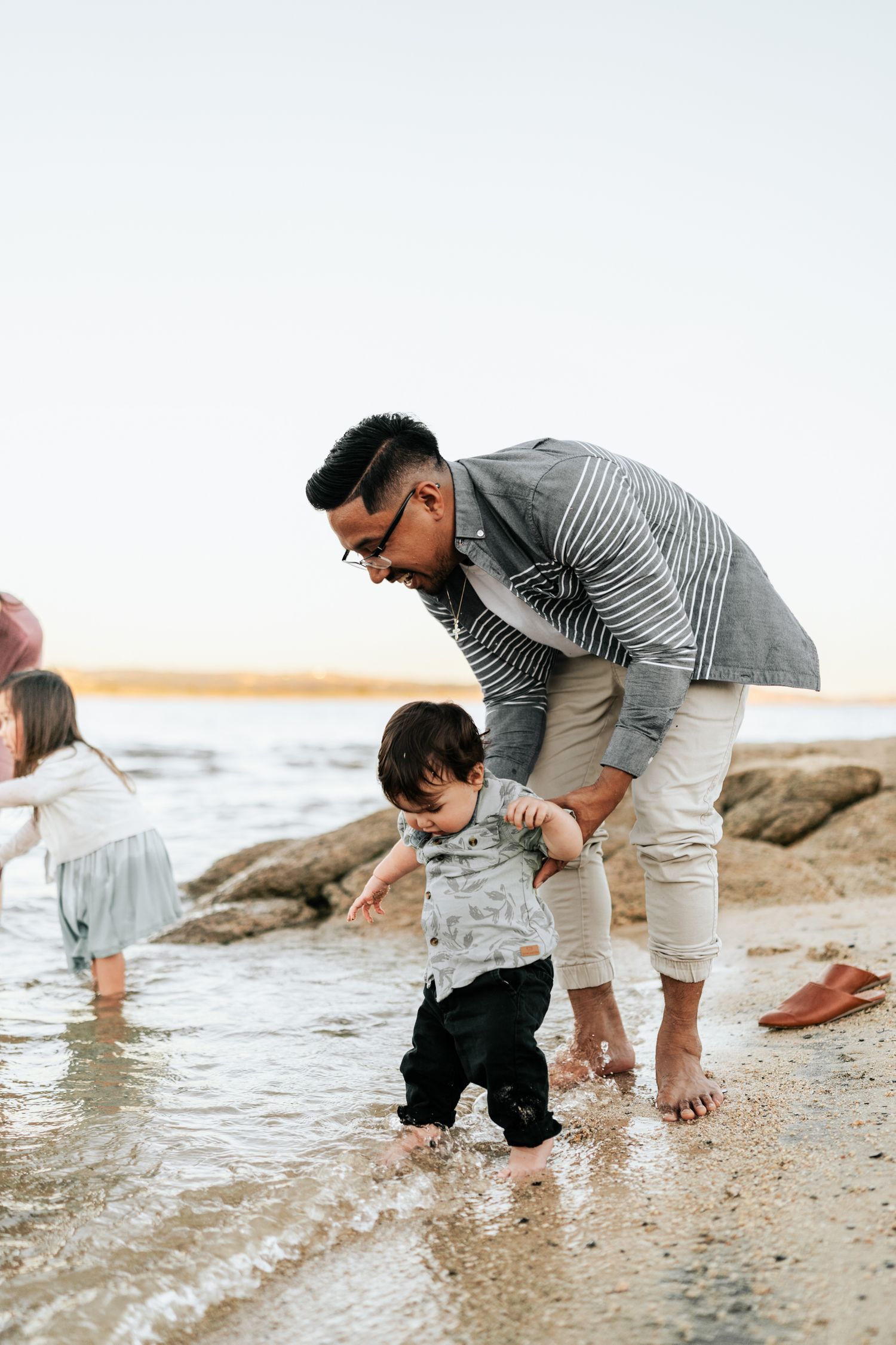 Family members exploring the shoreline and splashing in shallow water at the beach.