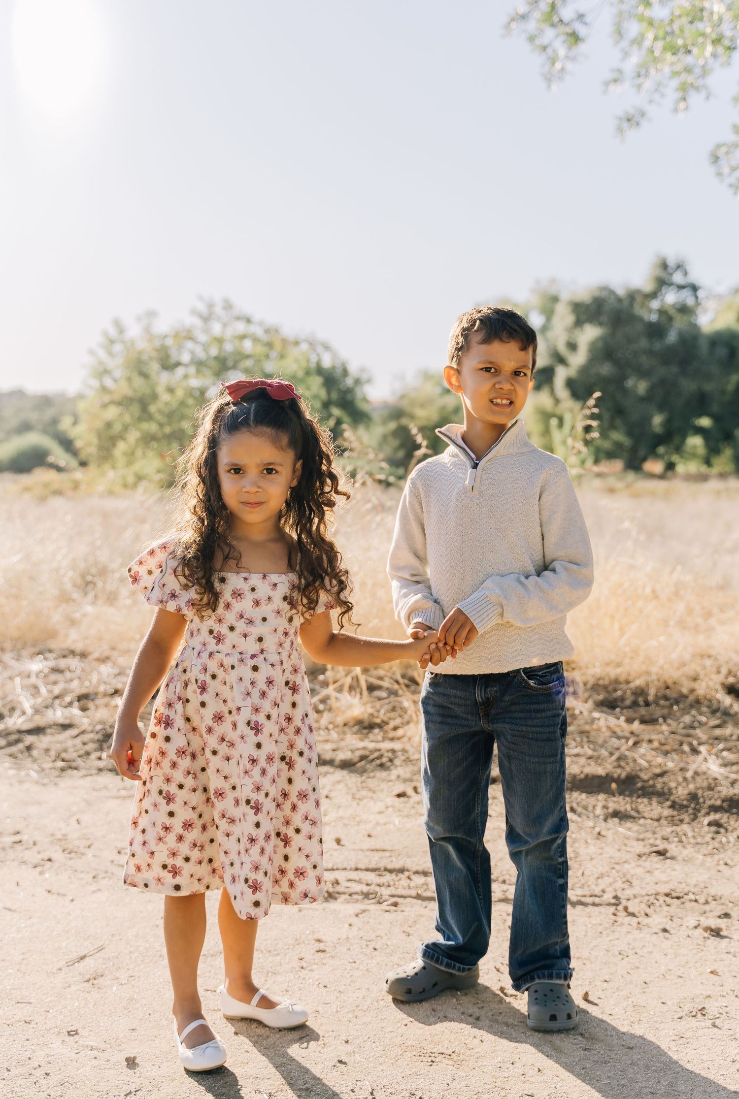 Two children playing and walking together on a dirt path in a sunlit field.