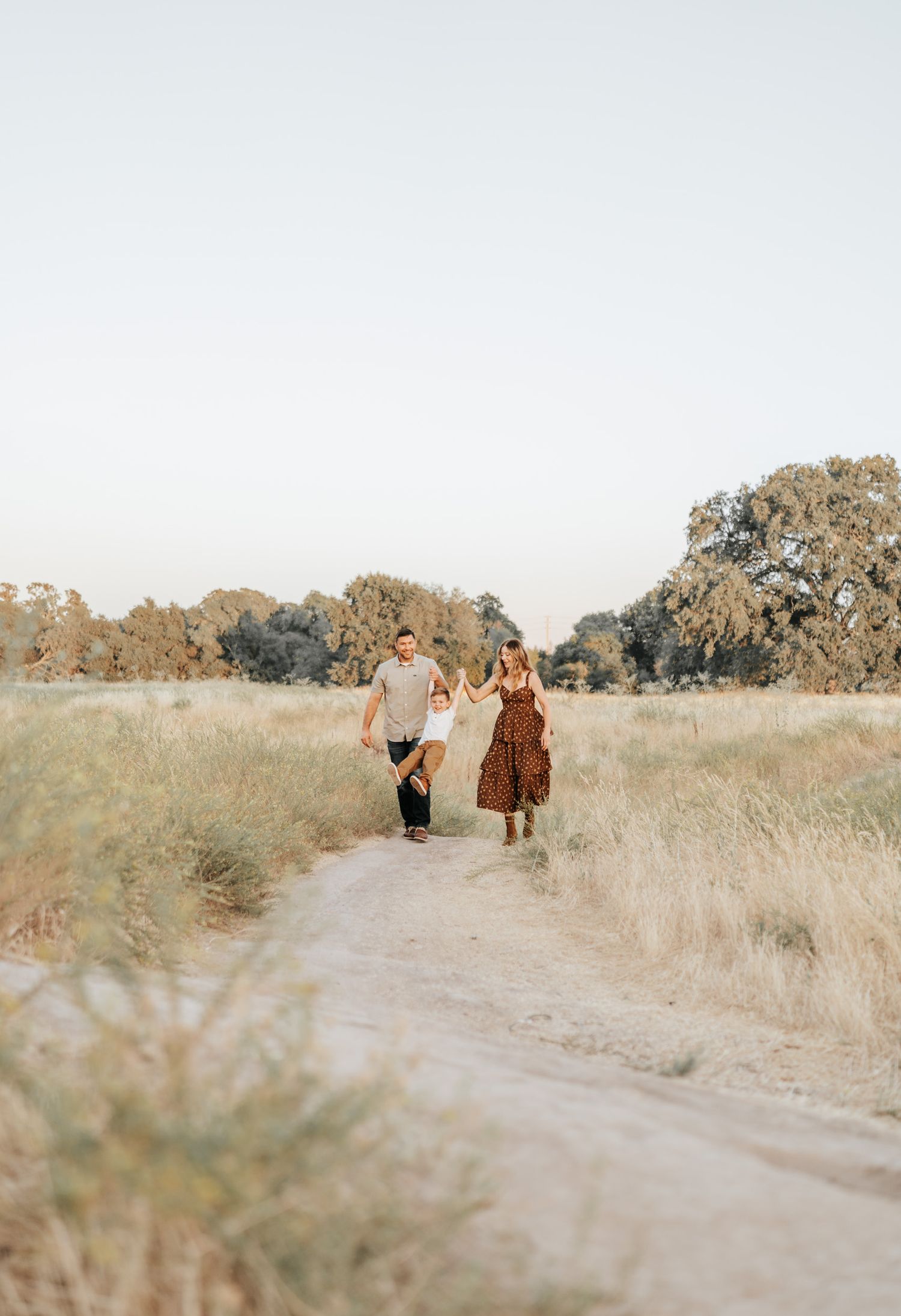 Family walking together on a winding dirt path through a sun-soaked meadow.