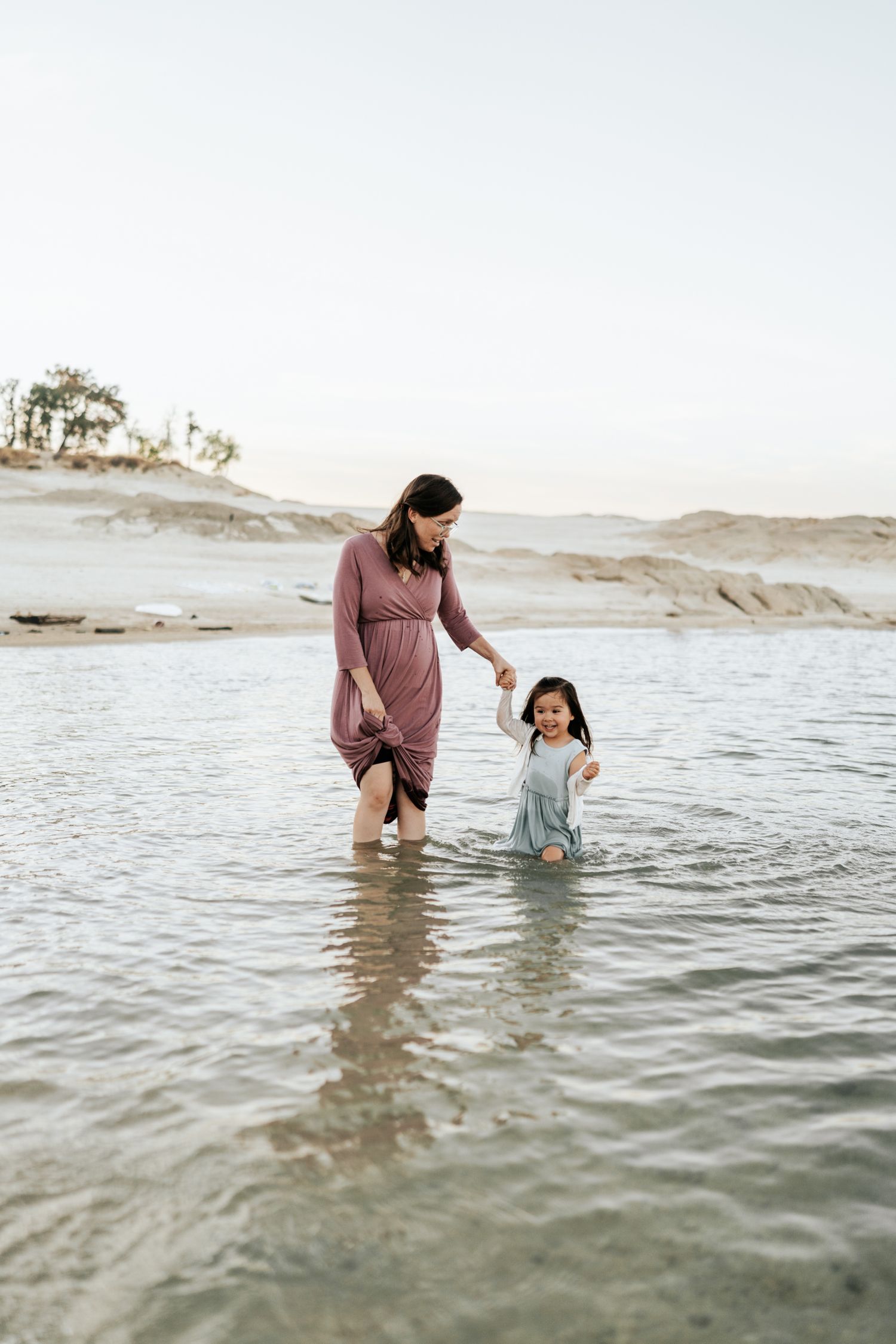 Two people wade together in shallow ocean water during a peaceful beach sunset.