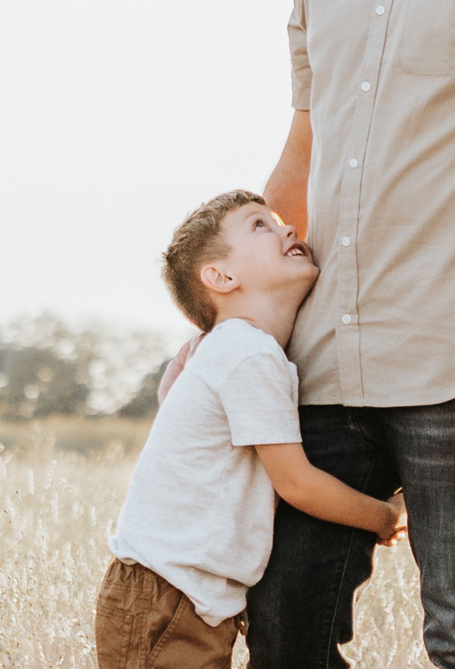 Child hugging parent's legs affectionately in a sunlit meadow.