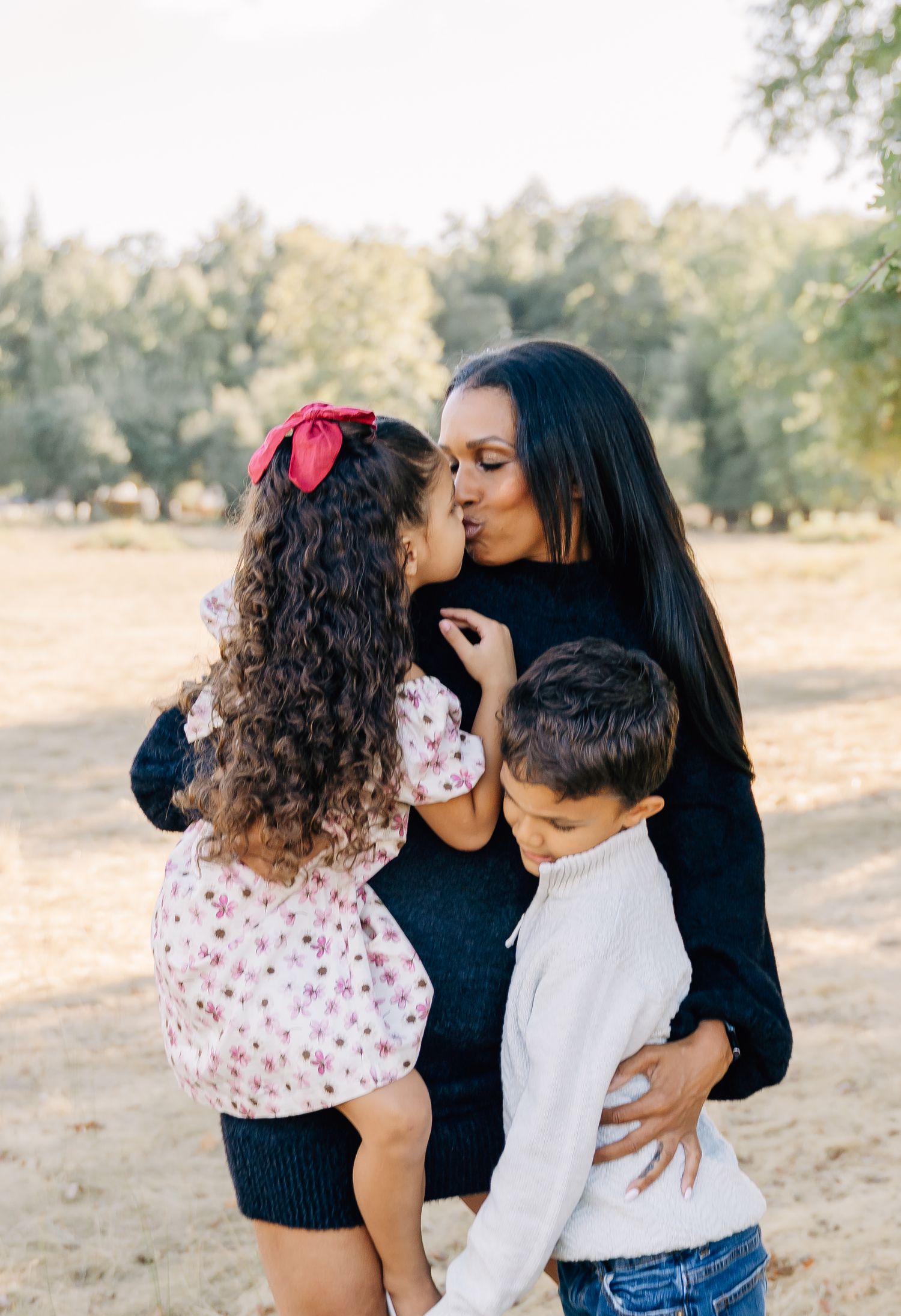 Intimate family moment captured showing tender kisses and embraces in a sunlit outdoor setting.