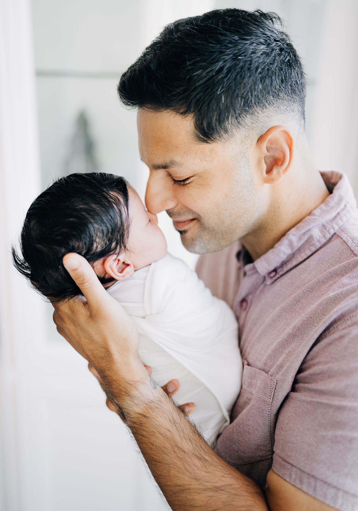 A father tenderly holds his newborn baby close, touching foreheads in an intimate bonding moment.