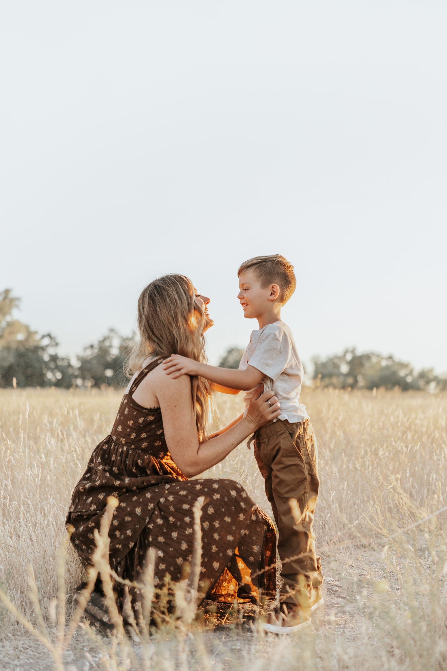Mother and son share tender moments together in a sunlit golden field at sunset.