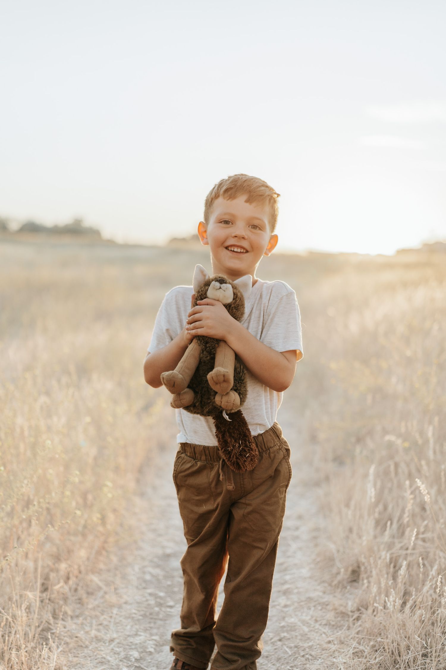 A joyful moment captured in a golden field at sunset with a small stuffed animal toy.