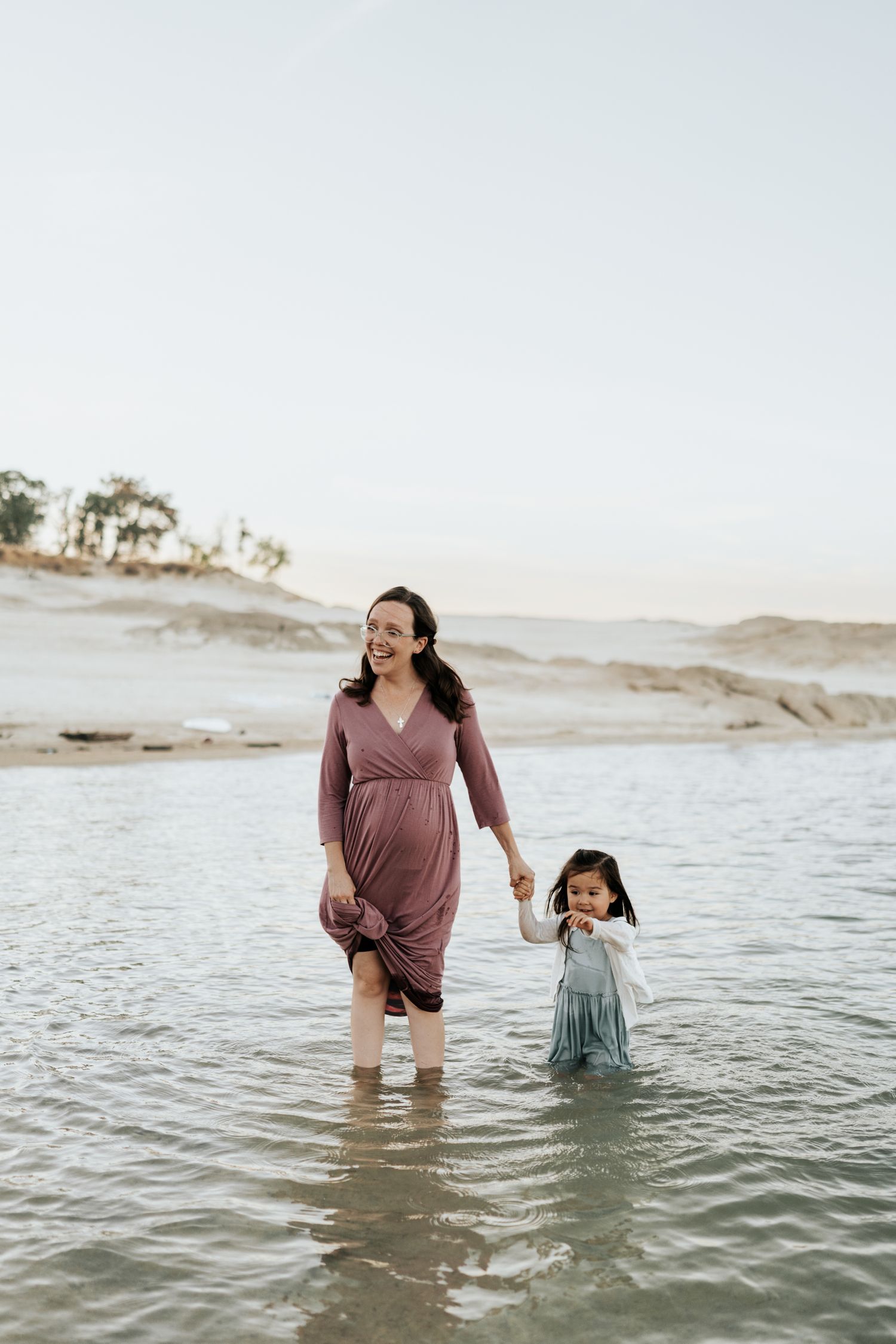 Parent and child playing together in ocean waves on a bright sunny day.