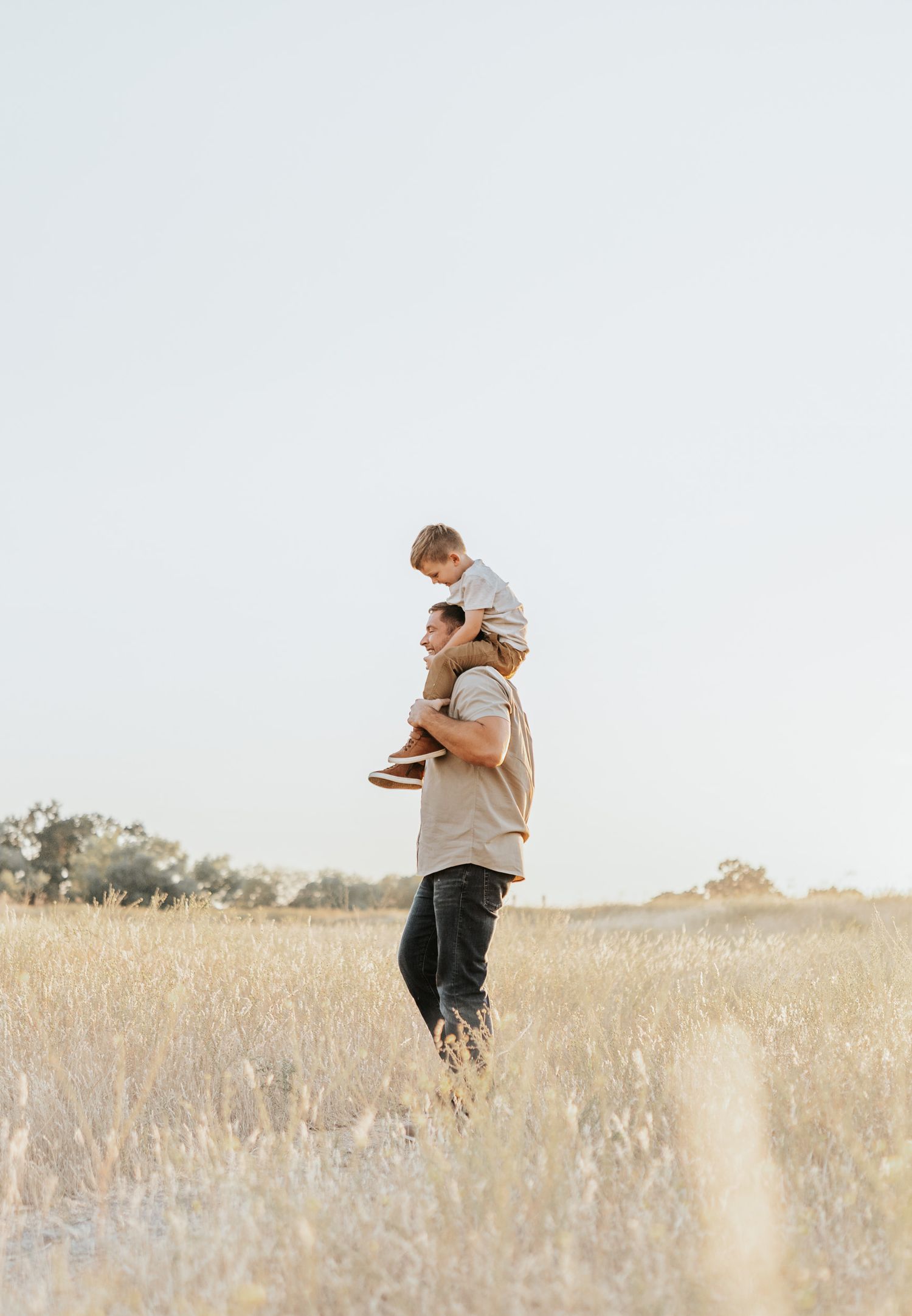 A child sits on an adult's shoulders in a peaceful field at dusk.