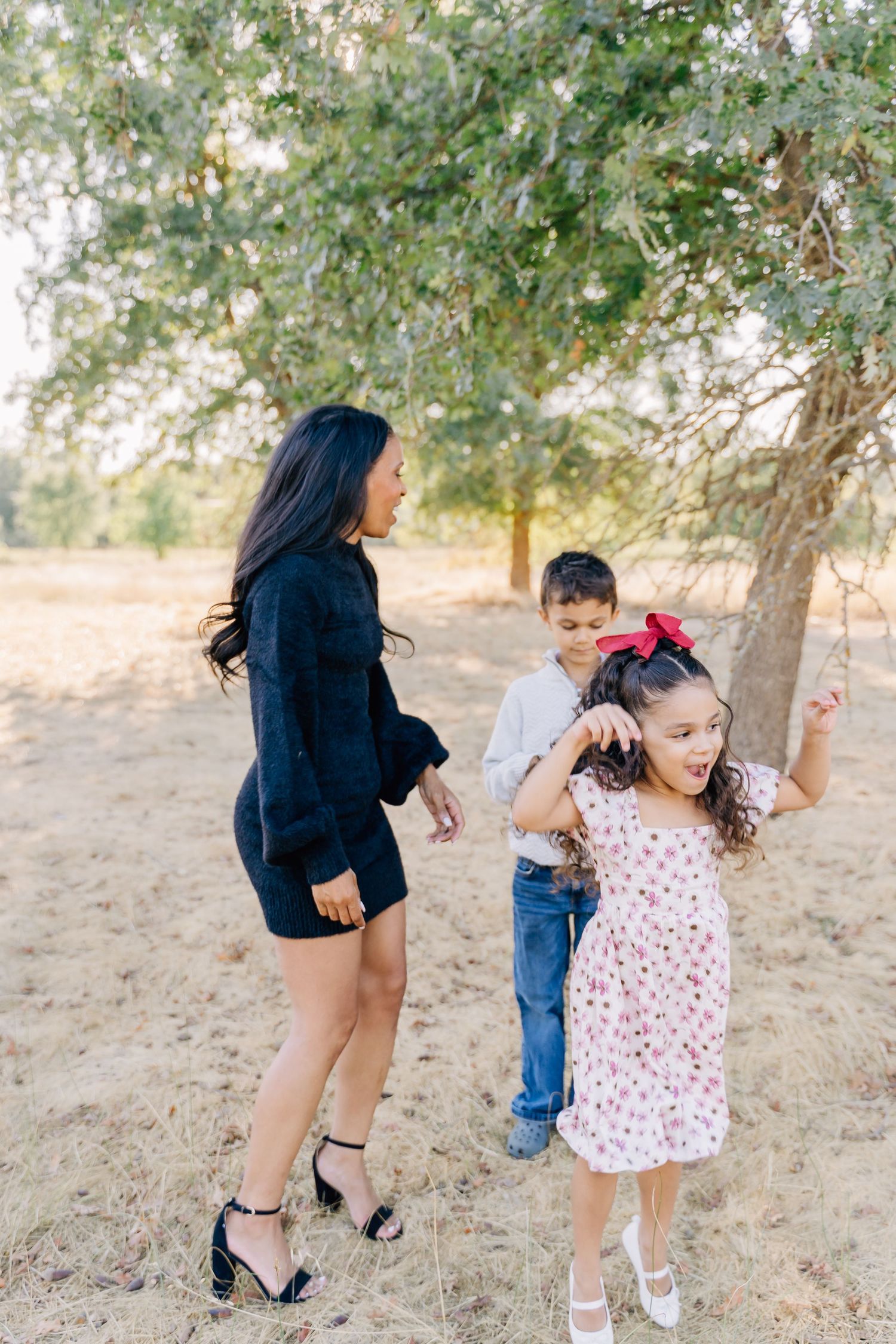 A playful sequence of people dancing and twirling together on a sunny hillside under trees.