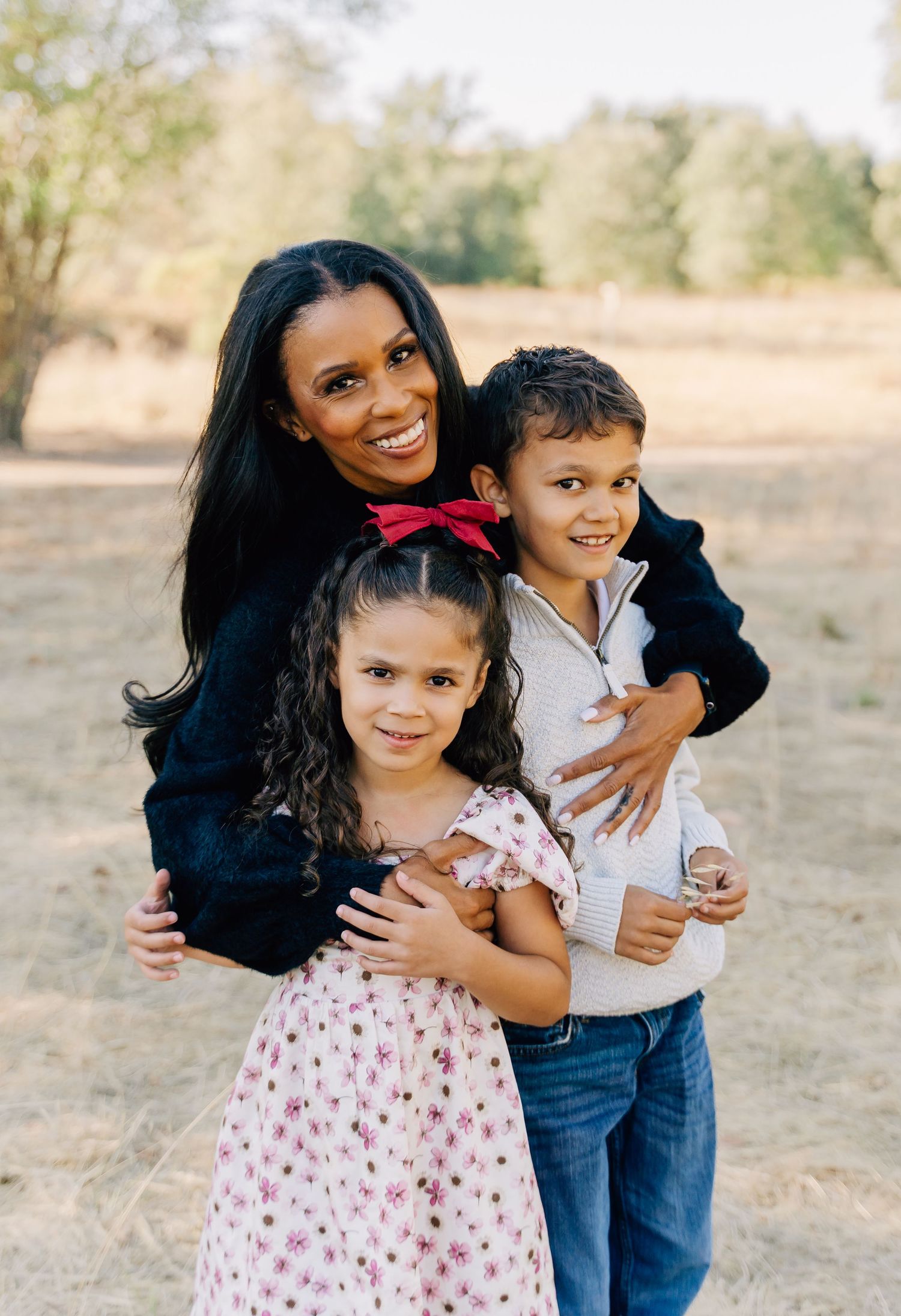 A joyful outdoor family photoshoot in a natural setting with warm sunlight and casual attire.