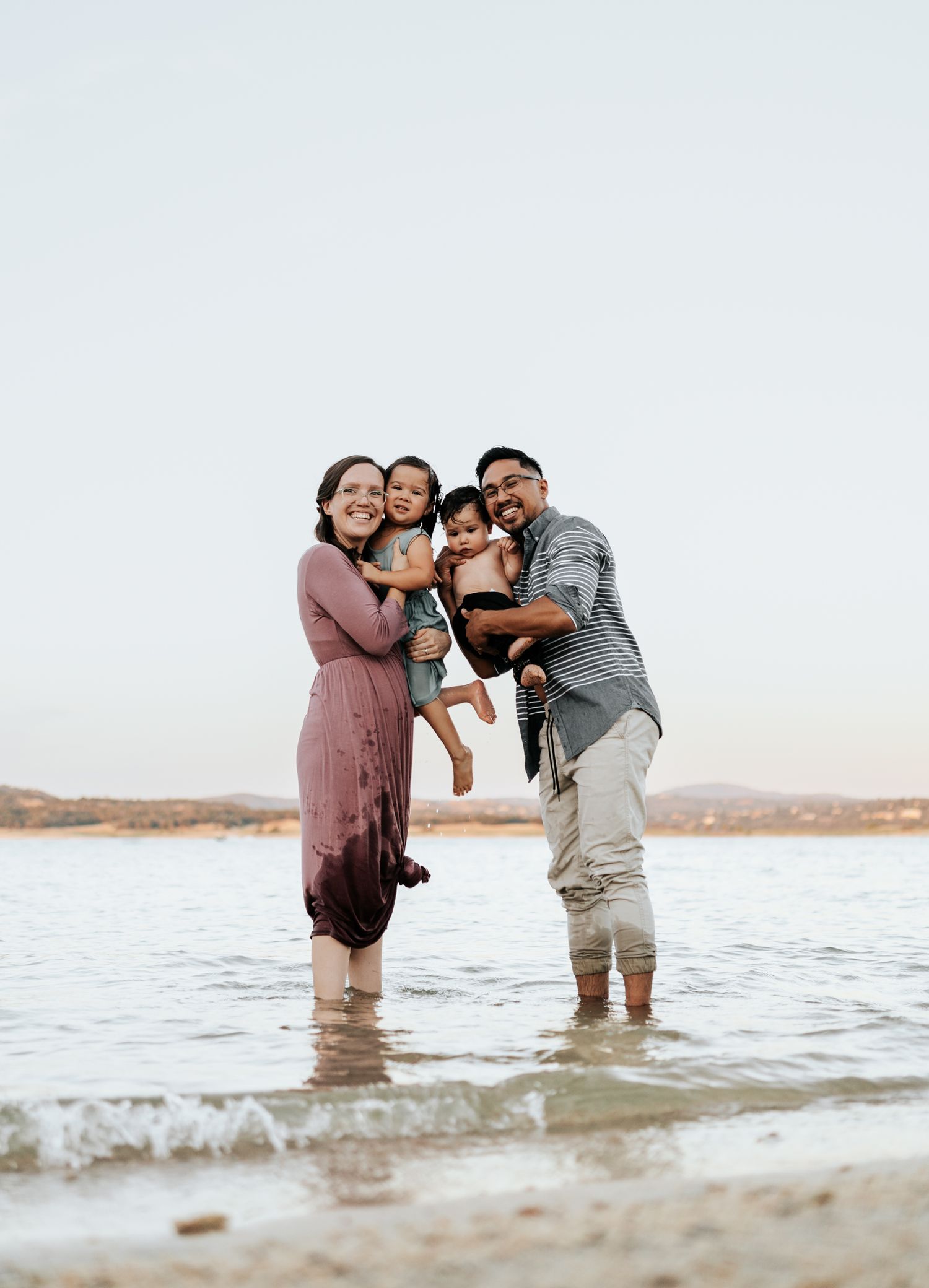 Family shares joyful moments playing together in shallow ocean waters at sunset.
