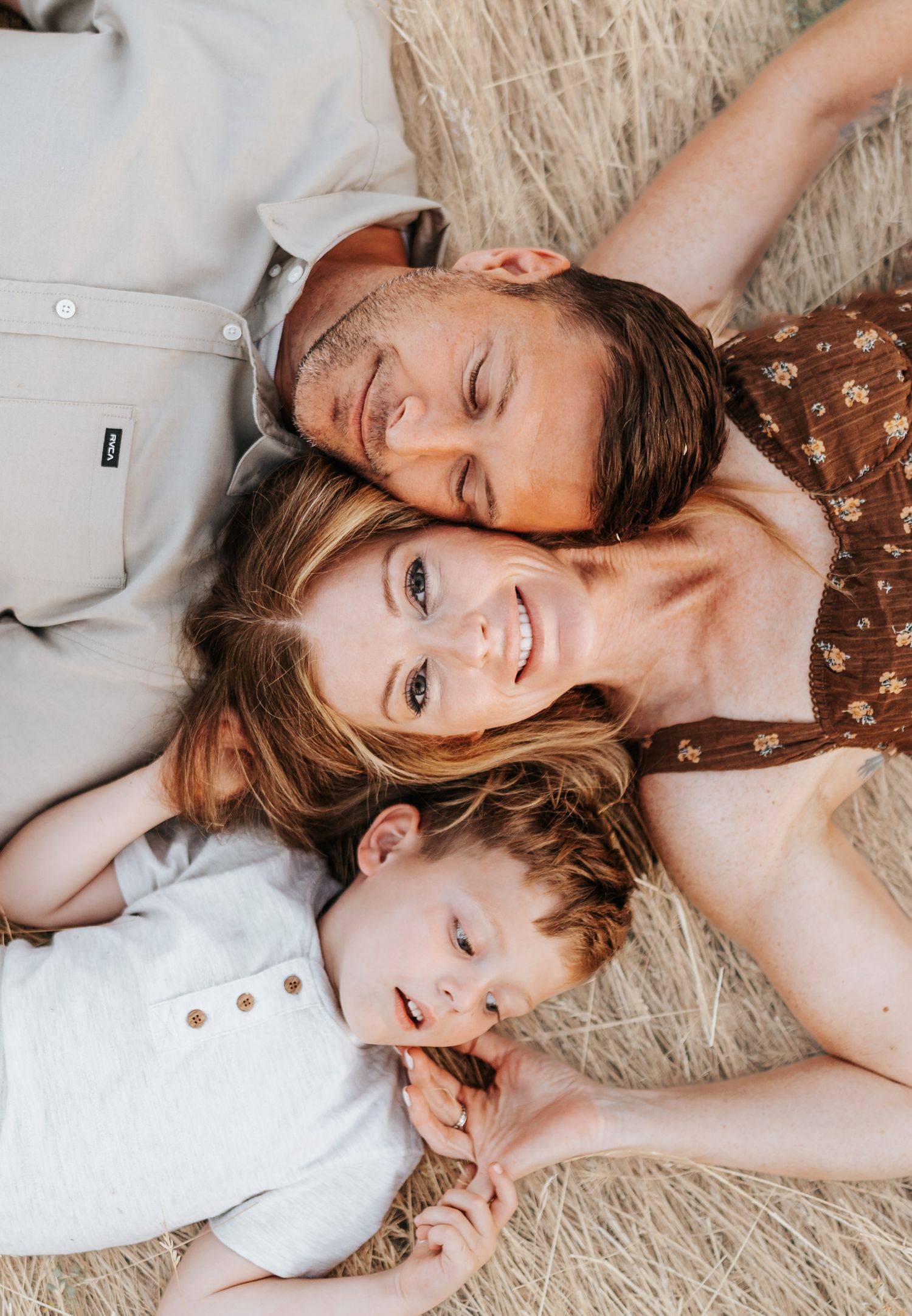 Family laying head-to-head in a circle on golden grass, sharing smiles and laughter.