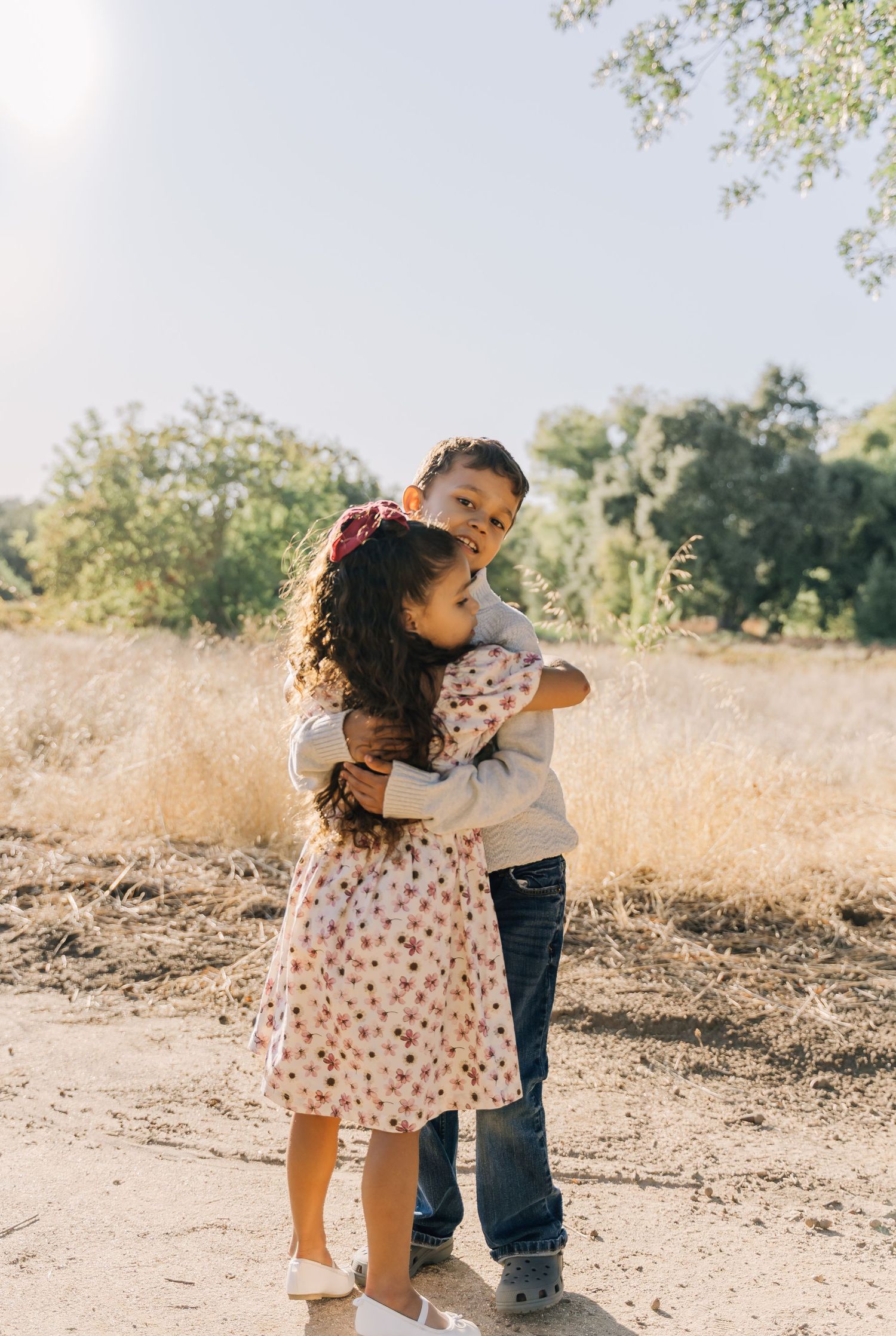Two children in casual clothes playing and hugging on a sunny dirt path.