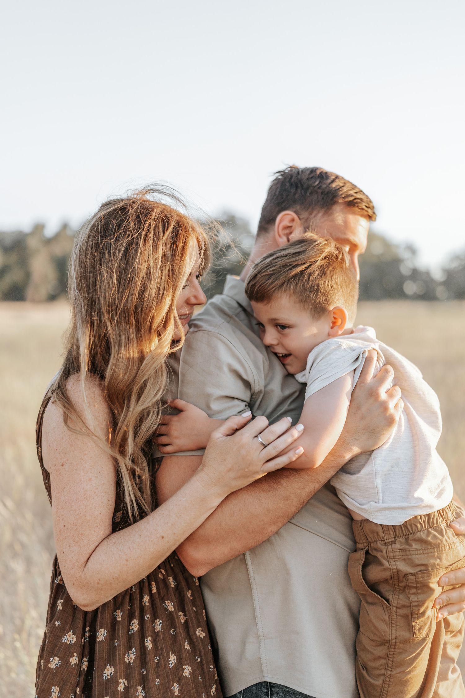 Mother and child embrace tenderly in golden sunlit field during intimate outdoor portrait session.