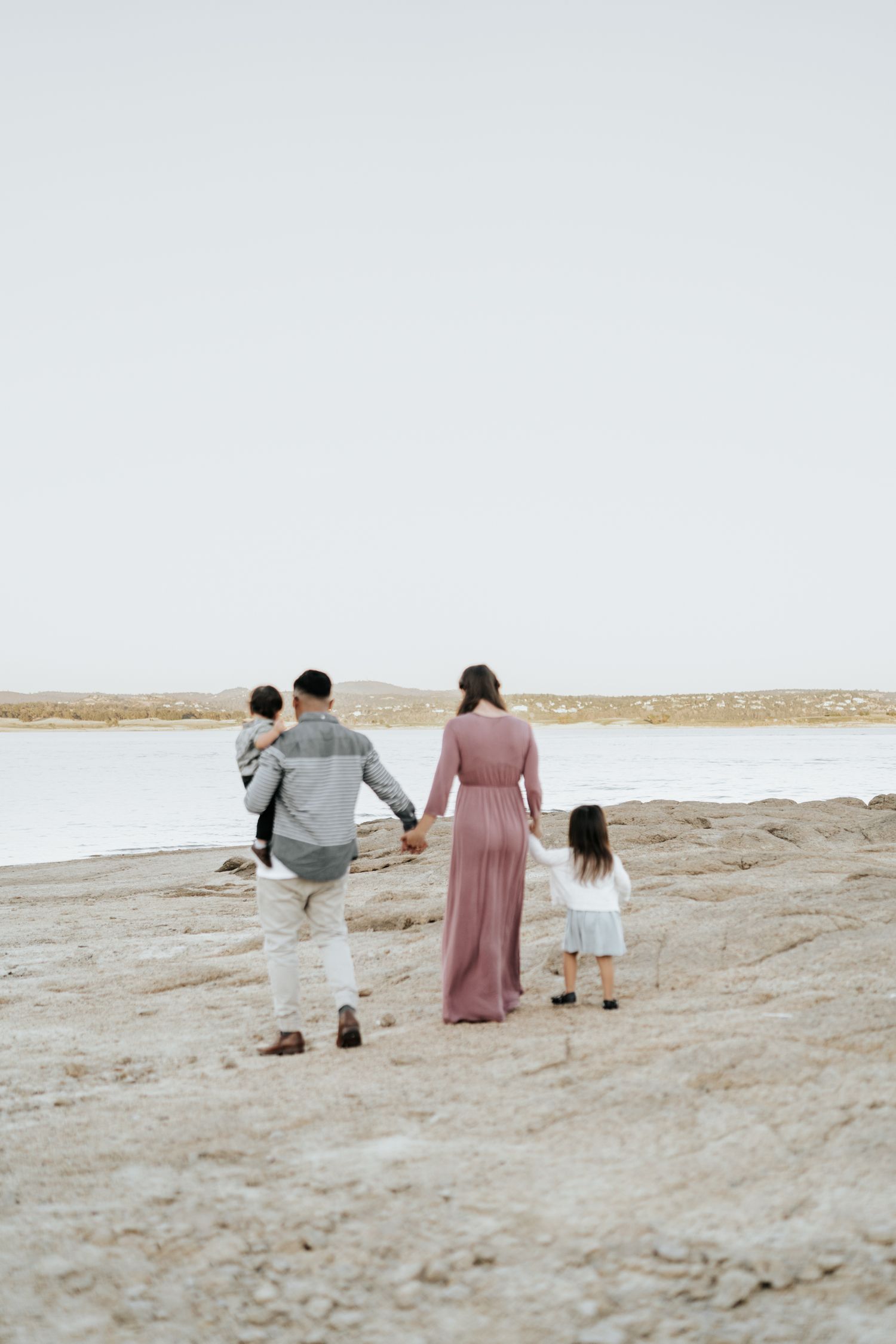 Family walking together on a sandy beach during golden hour, viewed from behind.