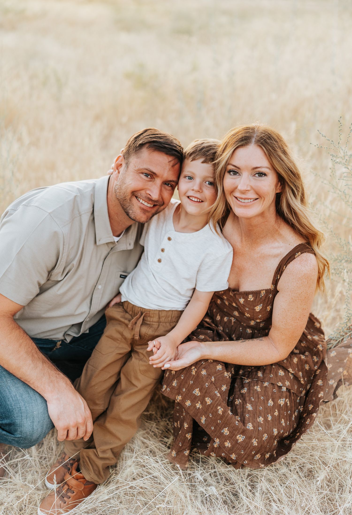 Family of three posing together in a golden field during sunset photoshoot.