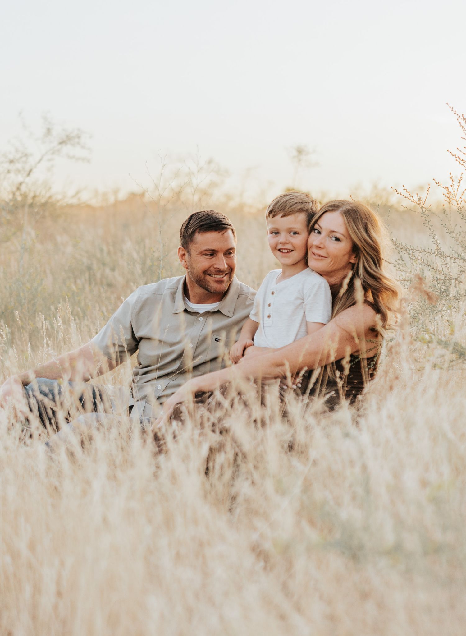 Family lying together in tall grass during golden hour sunset photo session.