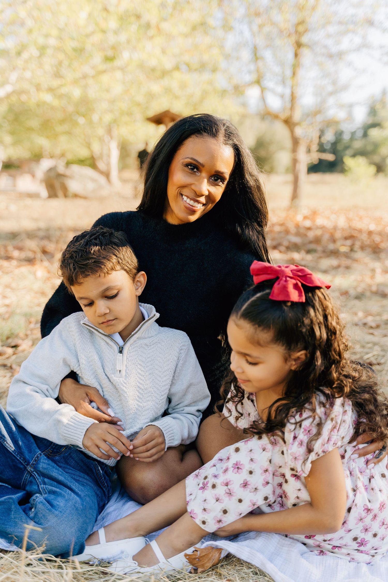 A family sits together on a blanket outdoors during autumn, sharing a tender moment in nature.