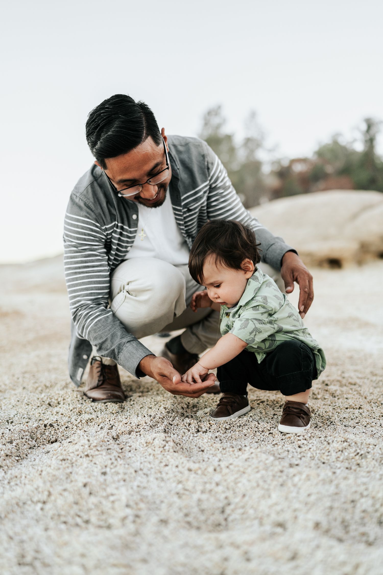 Adult in striped shirt crouched down showing child something on sandy ground in three sequential photos.