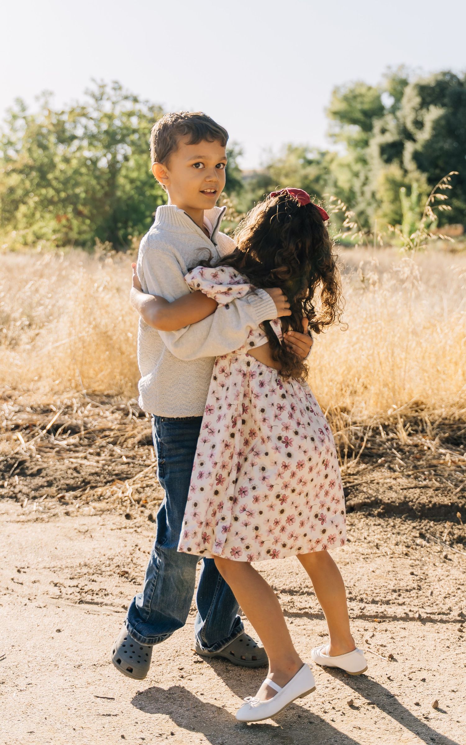 Two children play together in a golden field during sunset, wearing casual clothes and showing playful interaction.