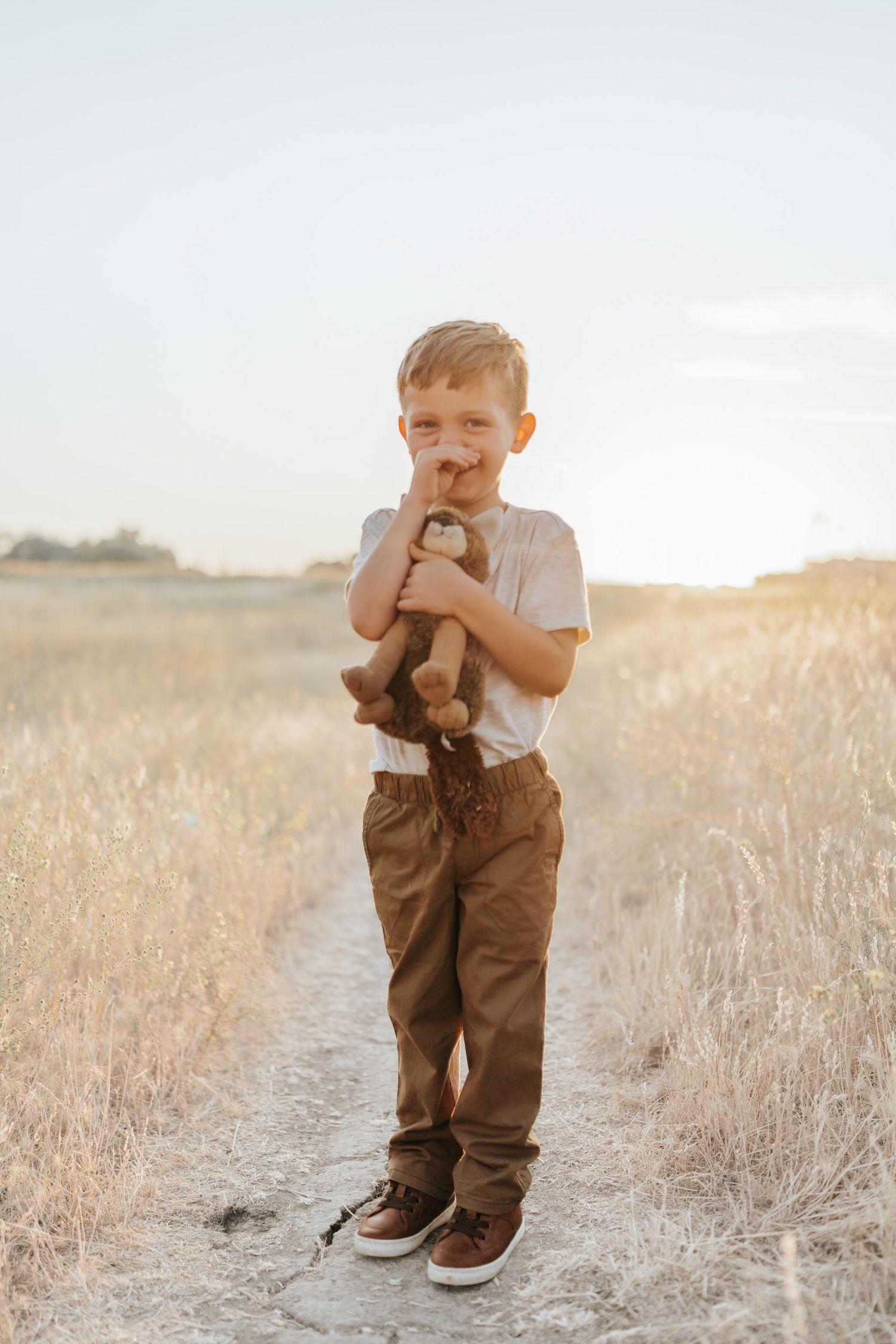 Young child playing in khaki overalls amid dry grass in golden afternoon light.