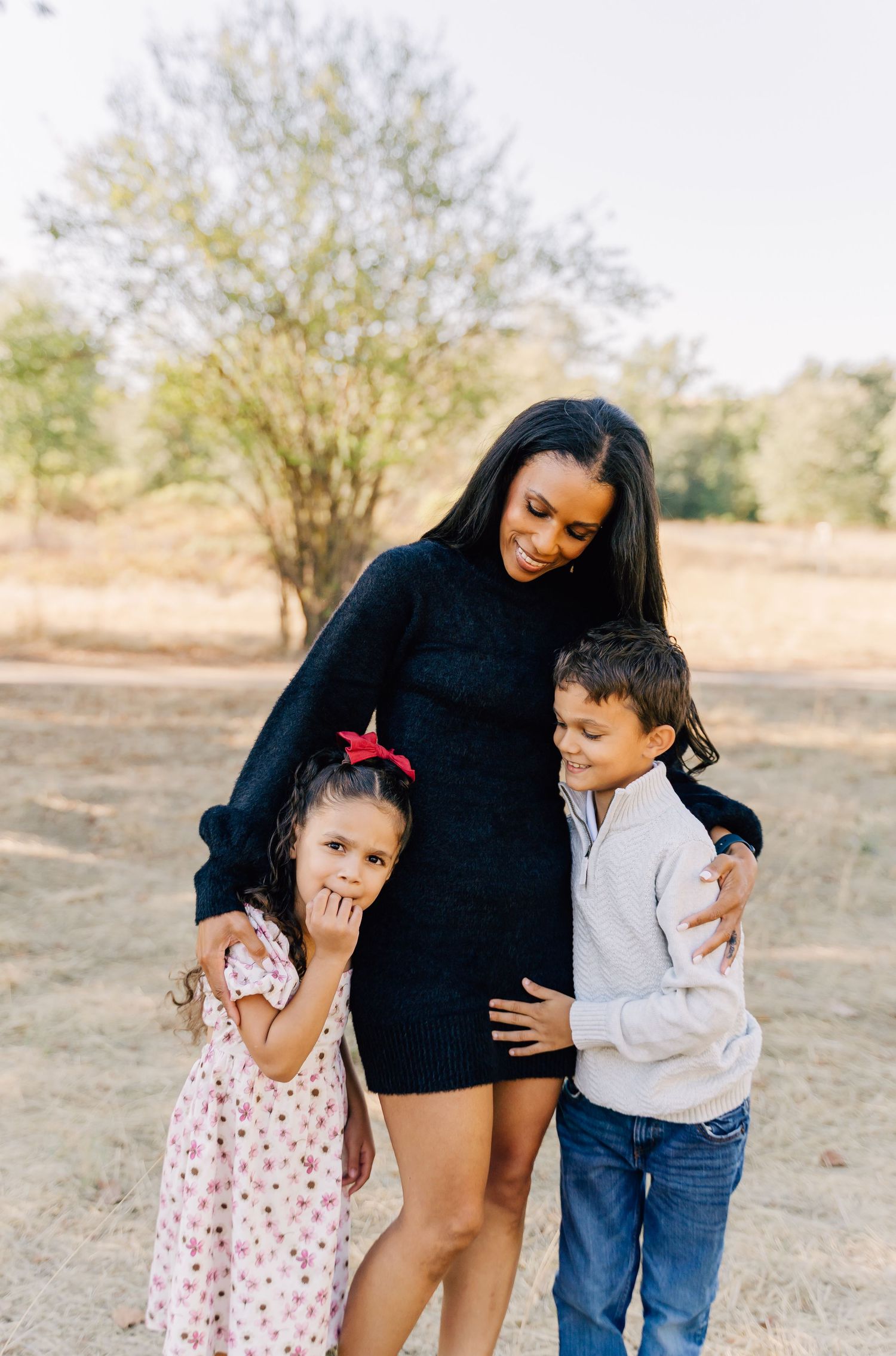 A touching outdoor family portrait showing warm embraces and smiles in a natural setting.