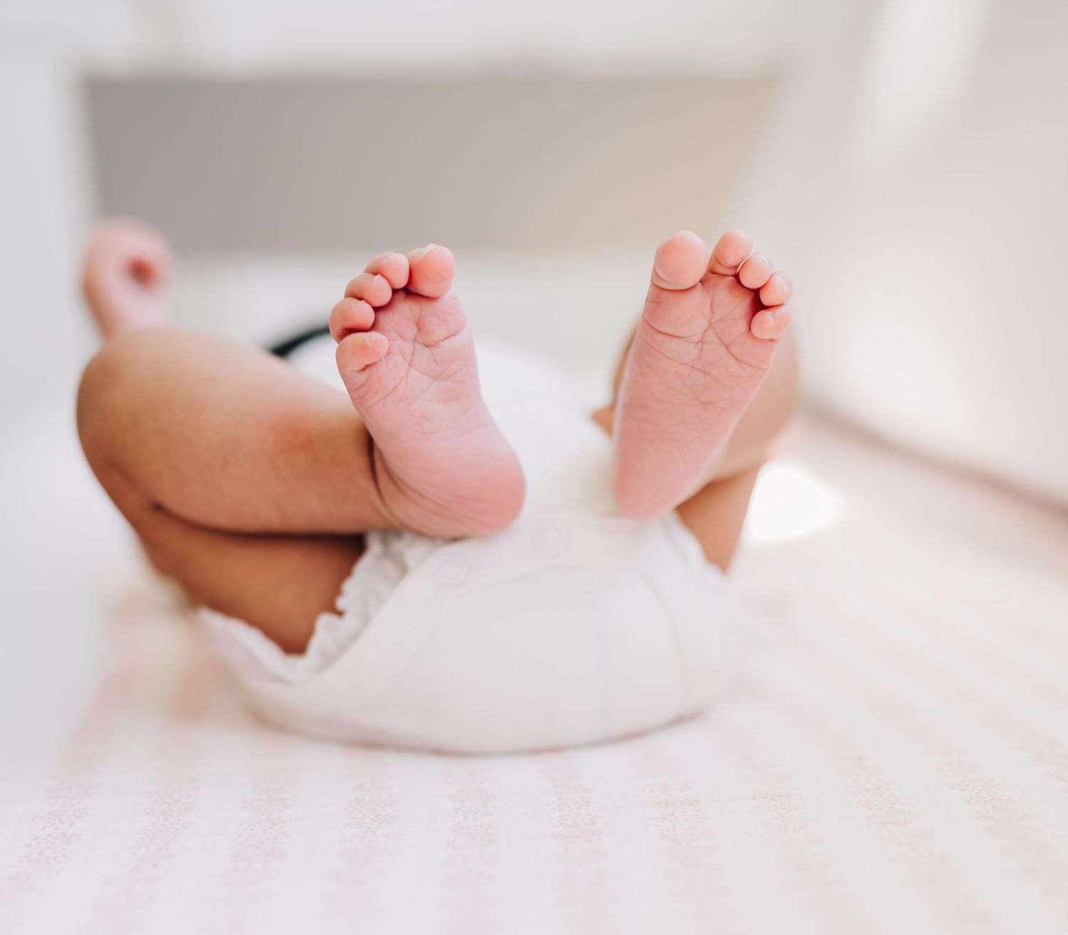 Close-up of newborn baby feet in a white diaper lying on a soft pink blanket.