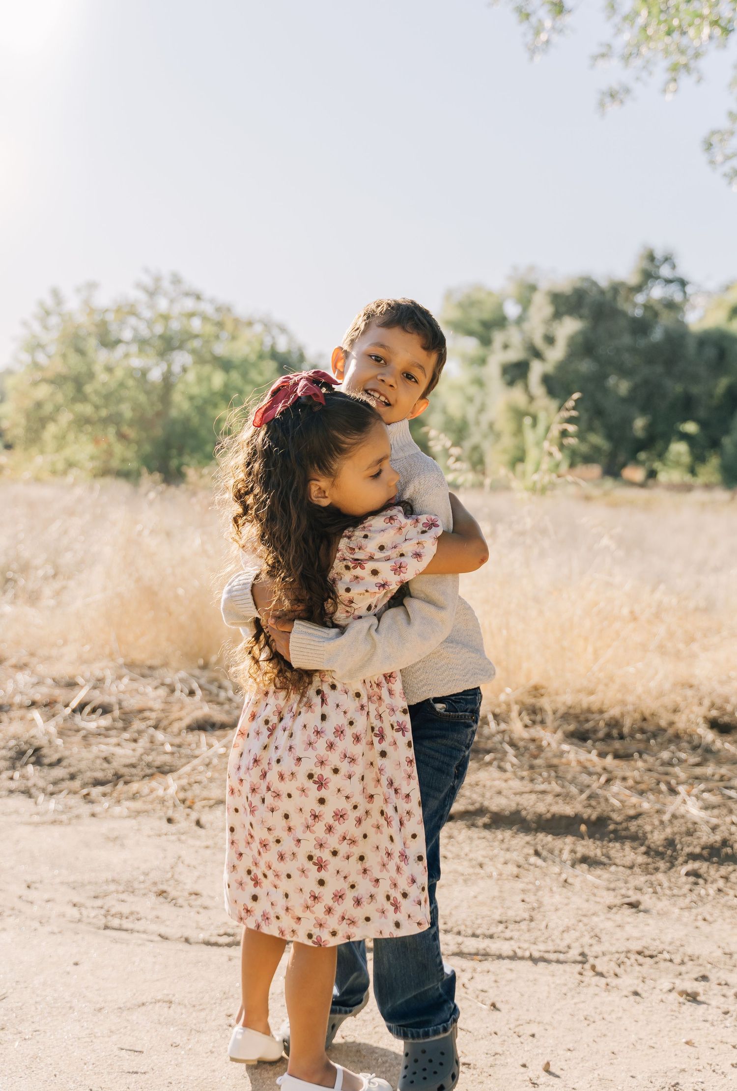Two young children share a sweet embrace while playing outdoors in the sunshine.