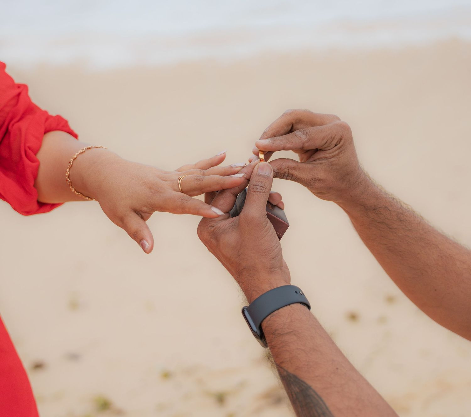 Close-up of hands exchanging a ring during a beach proposal.