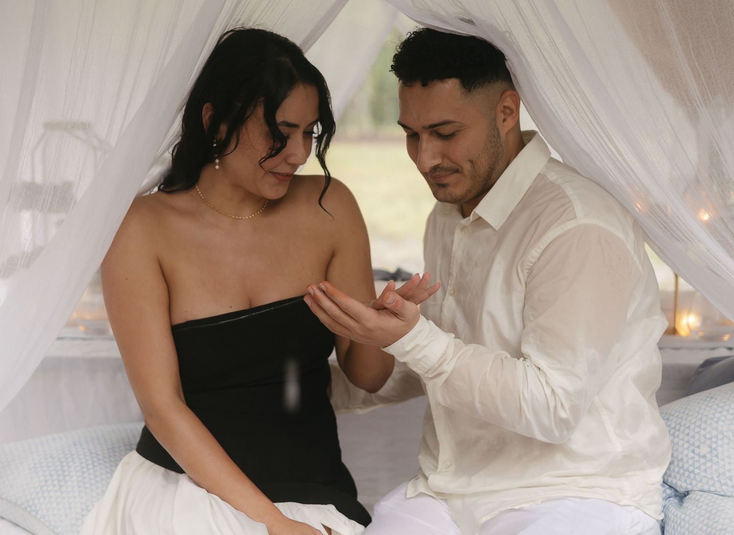 Couple in black and white attire sharing romantic moment under canopy.