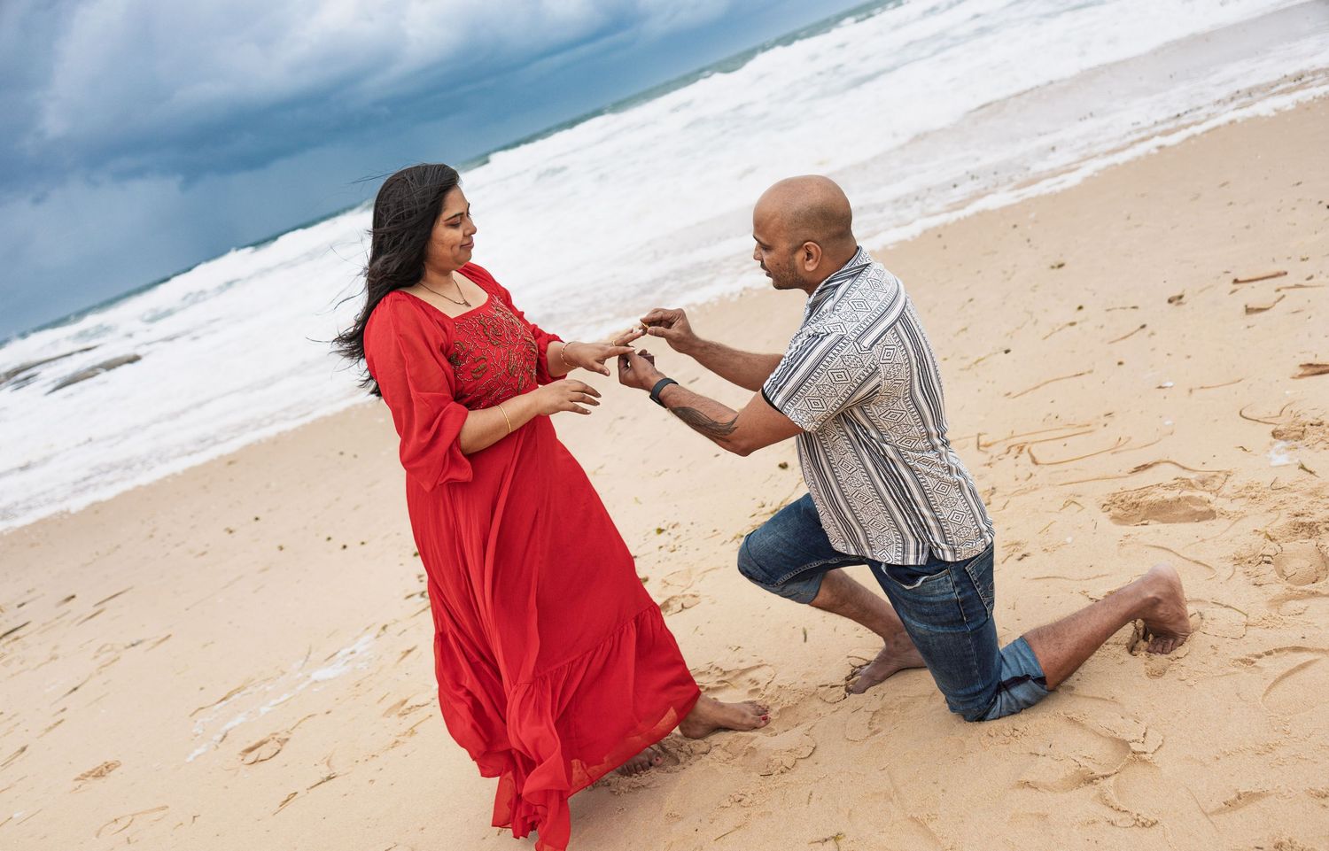 A romantic beach proposal scene with waves crashing in the background.