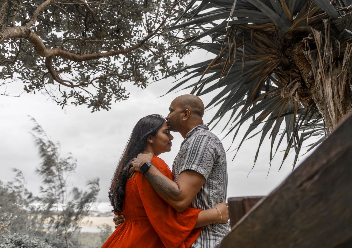 Romantic couple embracing under palm trees during an outdoor photoshoot.