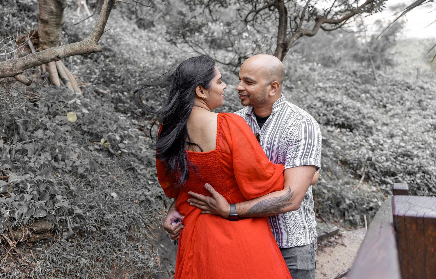 Intimate couple's portrait with woman in bright red dress against desaturated background.