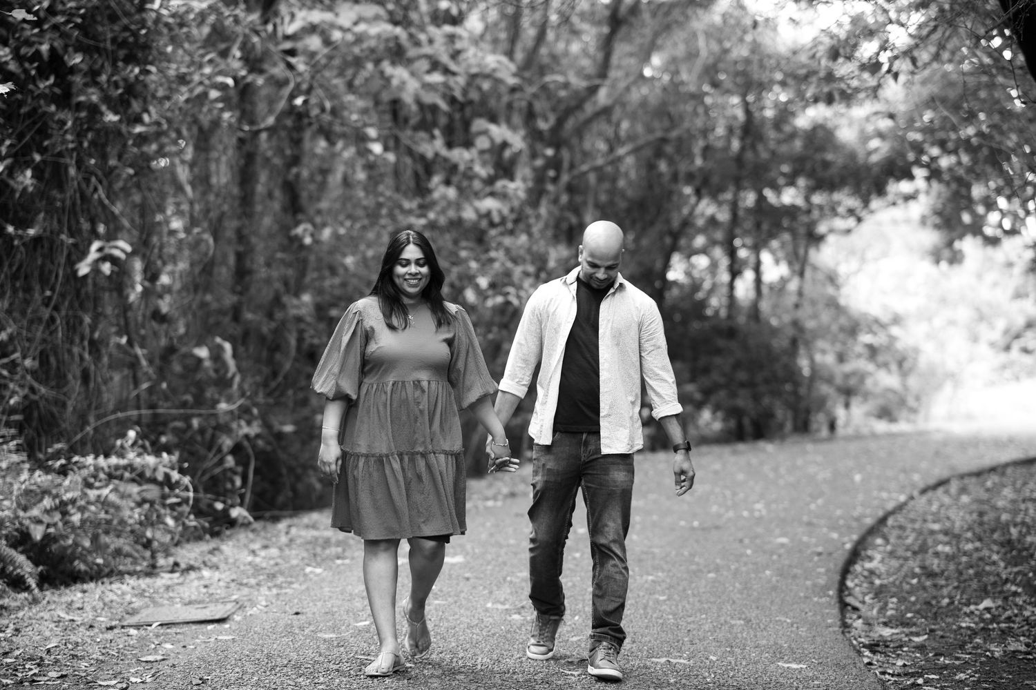 A couple walks hand in hand along a tree-lined path during an outdoor photoshoot.