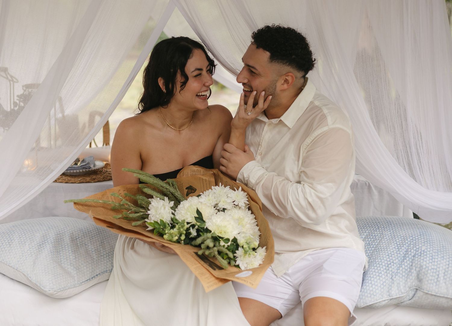 Tender romantic photoshoot under flowing white fabric with soft lighting.