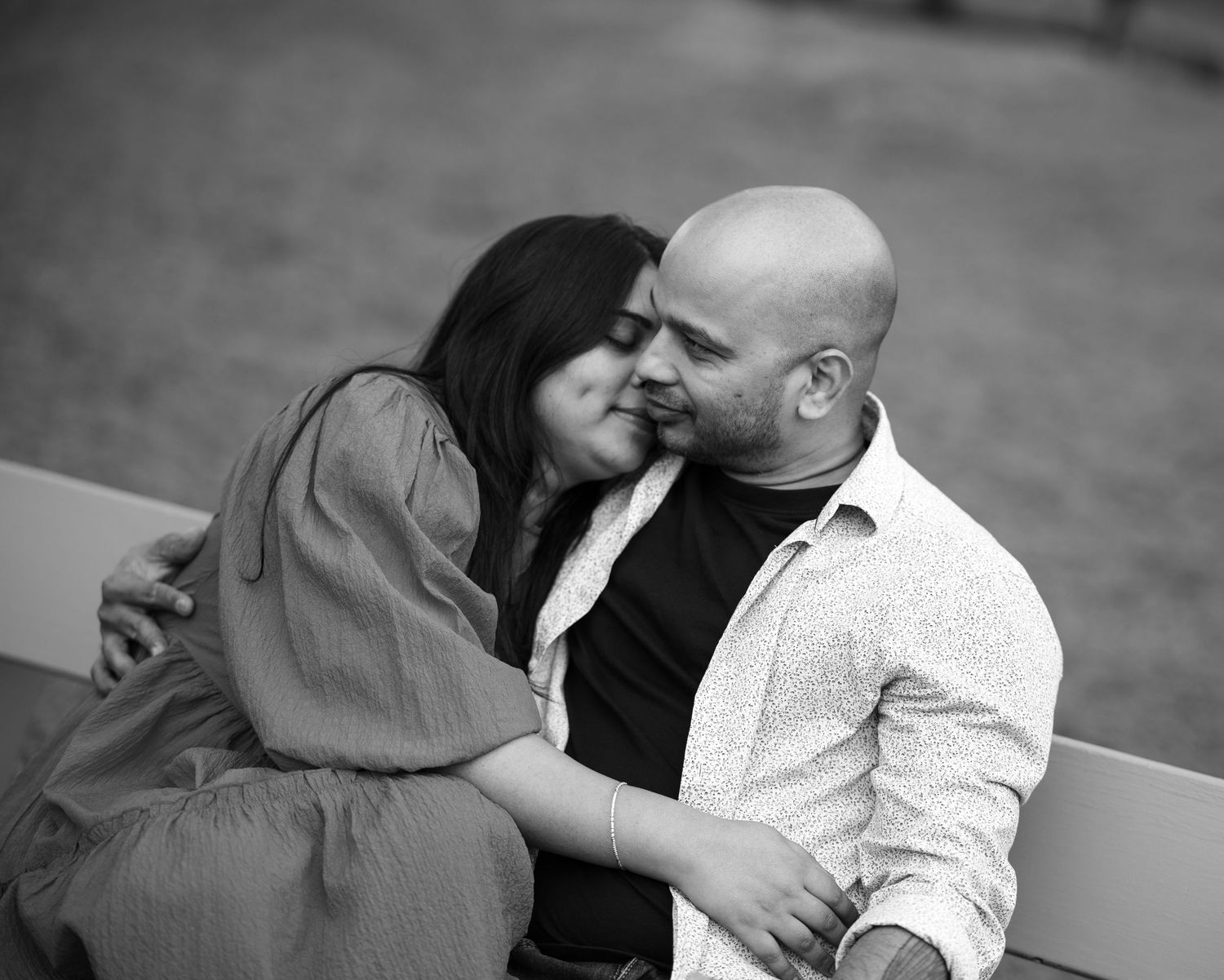 A couple snuggles close together on park benches during a black and white portrait session.
