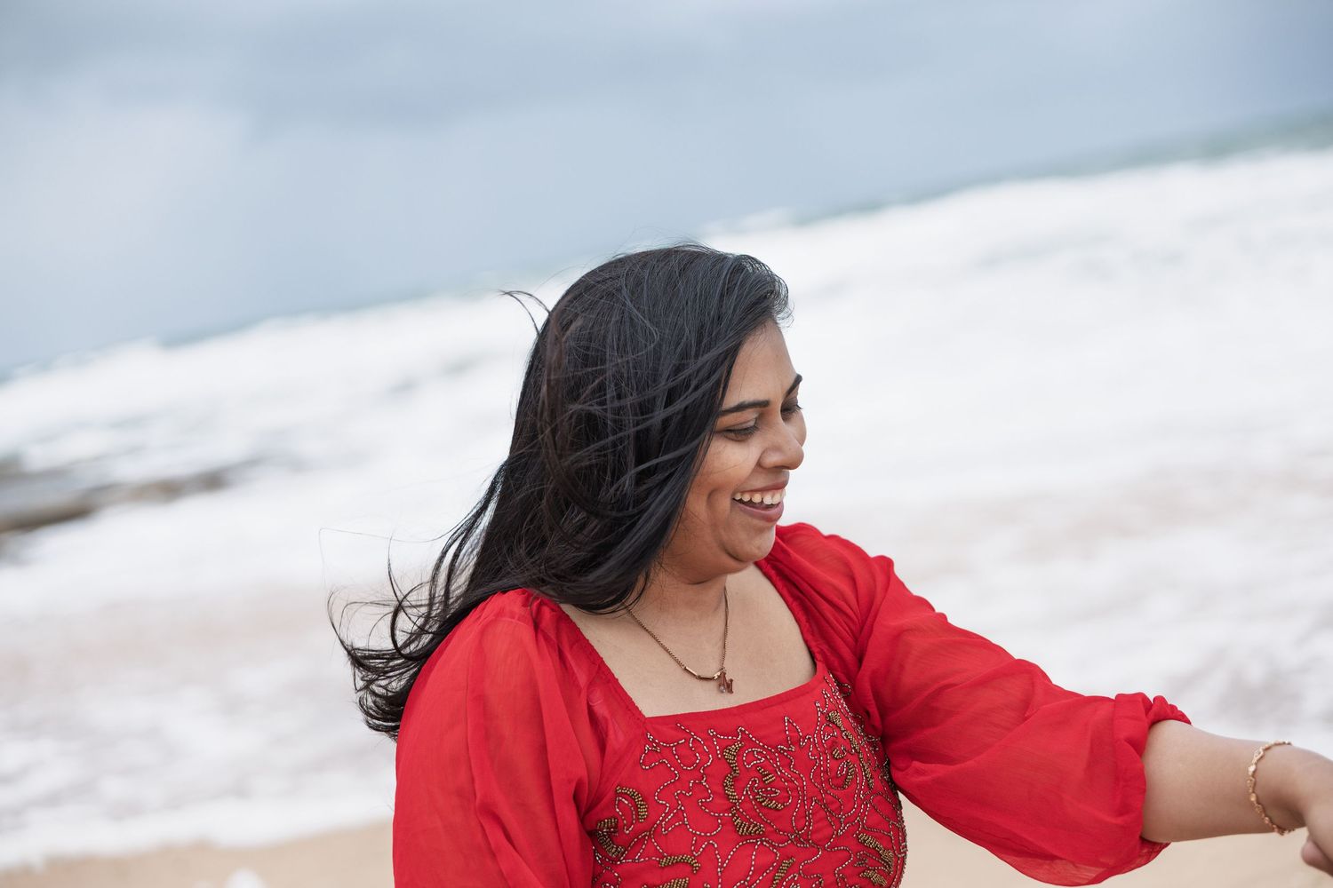 Joyful celebration moment after beach proposal with waves crashing behind.