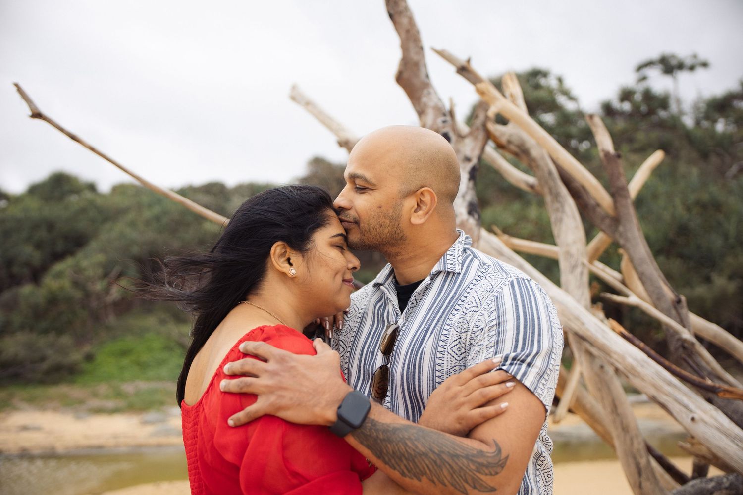 Romantic moment shared between couple near driftwood on a sandy beach.