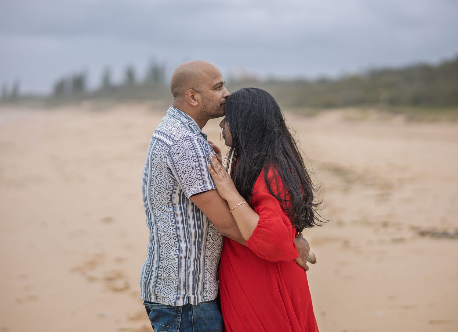 Intimate beach moment captured with couple embracing near ocean waves.