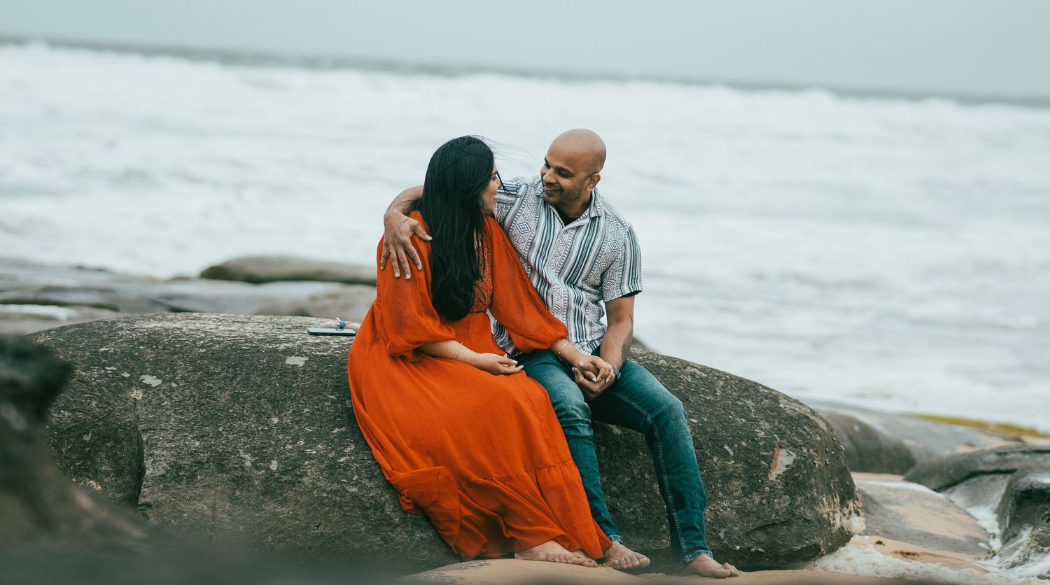 Panoramic beach scene with couple sitting together on coastal rocks.
