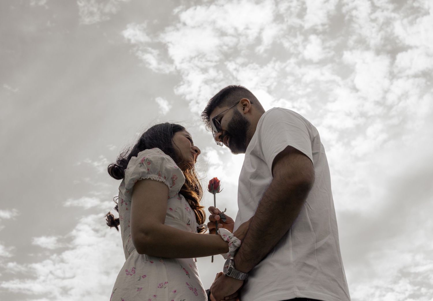 A couple shares a romantic moment during an outdoor engagement or wedding photoshoot against a cloudy sky.