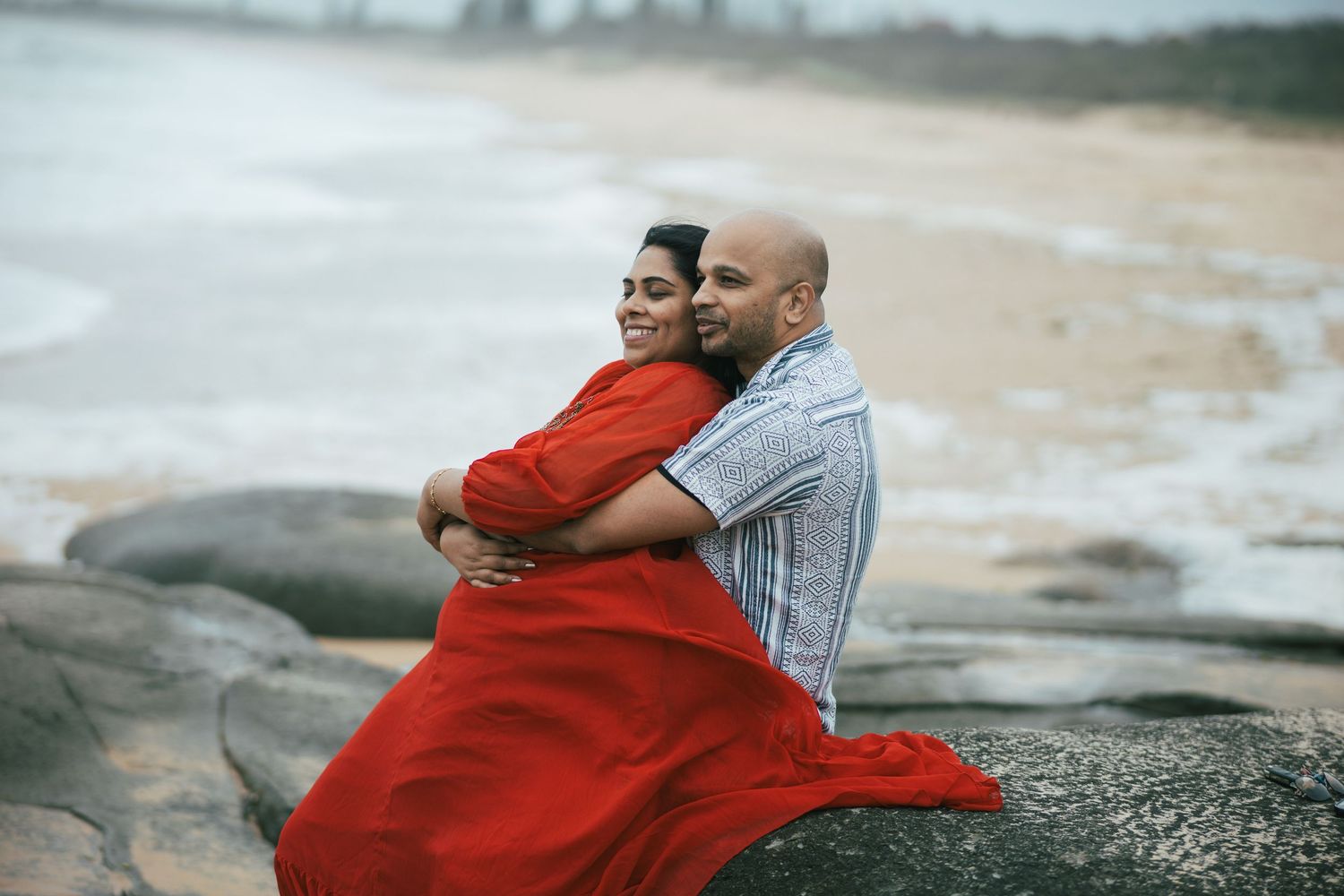 Romantic beach photography session with couple against rocky coastal backdrop.