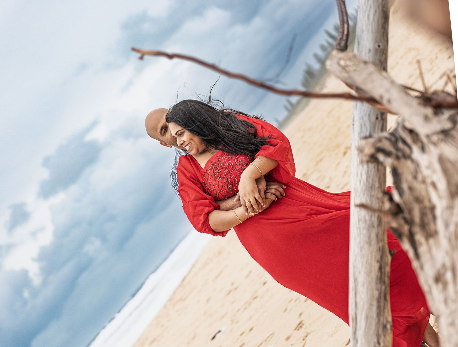 Candid beach photo with couple sharing romantic moment near driftwood.