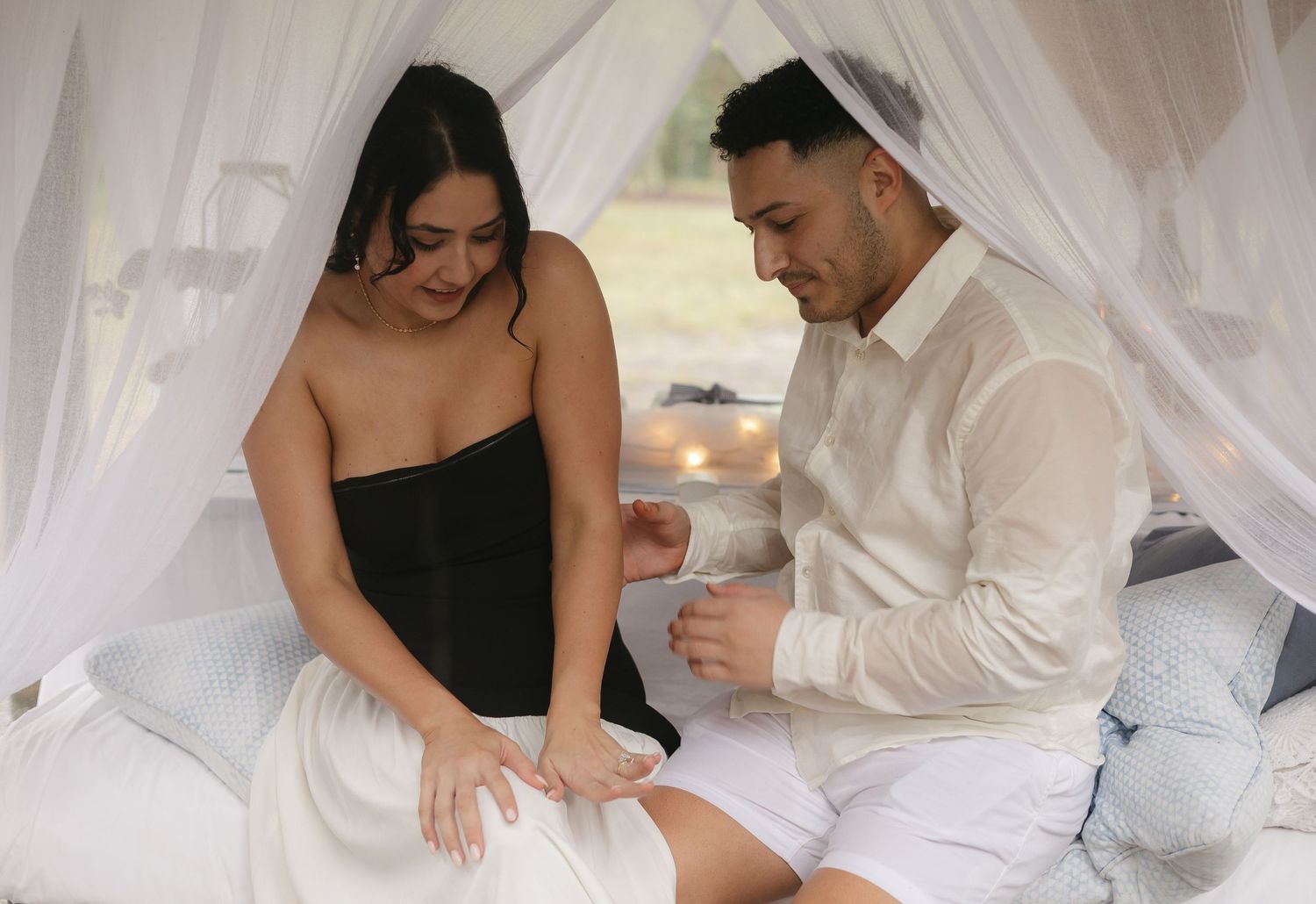 Couple lounging together under flowing white canopy in romantic setting.