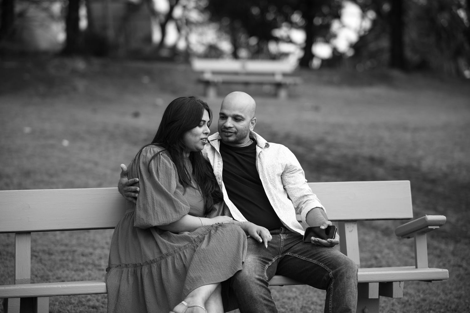 A couple embraces while sitting on park benches during a black and white photoshoot.