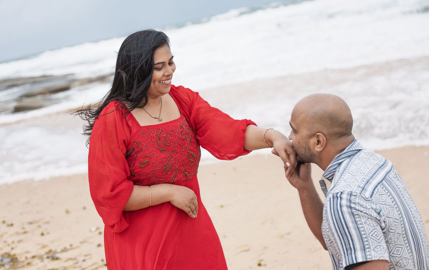 A proposal moment captured on a beach with ocean waves in the background.